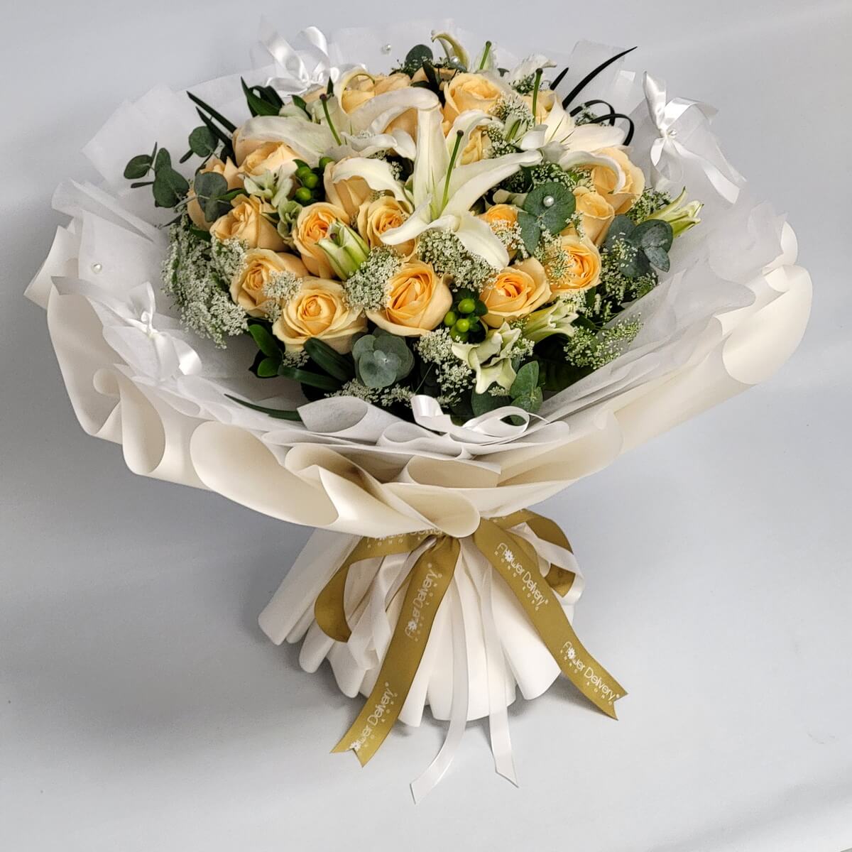 A bouquet of champagne-colored roses and white lilies, accented with greenery and delicate fillers, wrapped in layered white paper. 香檳玫瑰與白百合搭配綠葉與襯花，純白包裝展現優雅氣質。