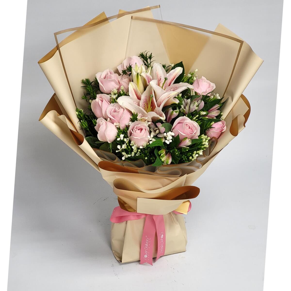 Wrapped bouquet of pink oriental lilies, pale pink roses, white filler flowers, and assorted foliage in beige wrapping 粉紅東方百合、淺粉玫瑰、白色配花與多種綠葉，包裝於米色紙中的花束