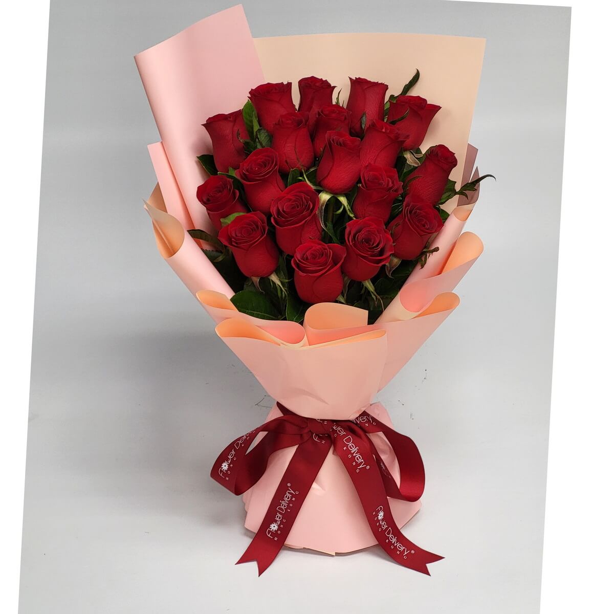 Full bouquet of long-stemmed red roses arranged with glossy green leaves, wrapped in soft pink paper and tied with a red ribbon - 長莖紅玫瑰與亮綠葉混合成束，淡粉紙包裝配紅絲帶