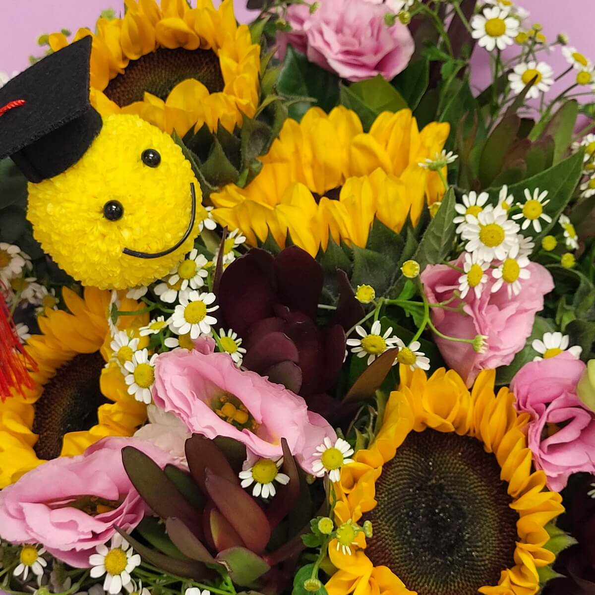 Graduation-themed bouquet featuring smiley yellow button chrysanthemum with black cap, sunflowers, pink lisianthus, white chamomile daisies, and mixed foliage 畢業主題花束含笑臉乒乓菊戴黑帽，搭配向日葵、粉紅洋桔梗、白洋甘菊與混合葉材