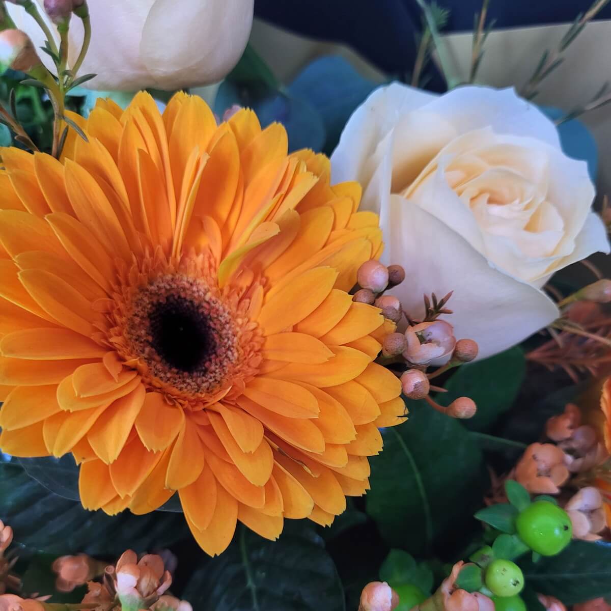 Close-up of an orange flower and a champagne rose in a bouquet.