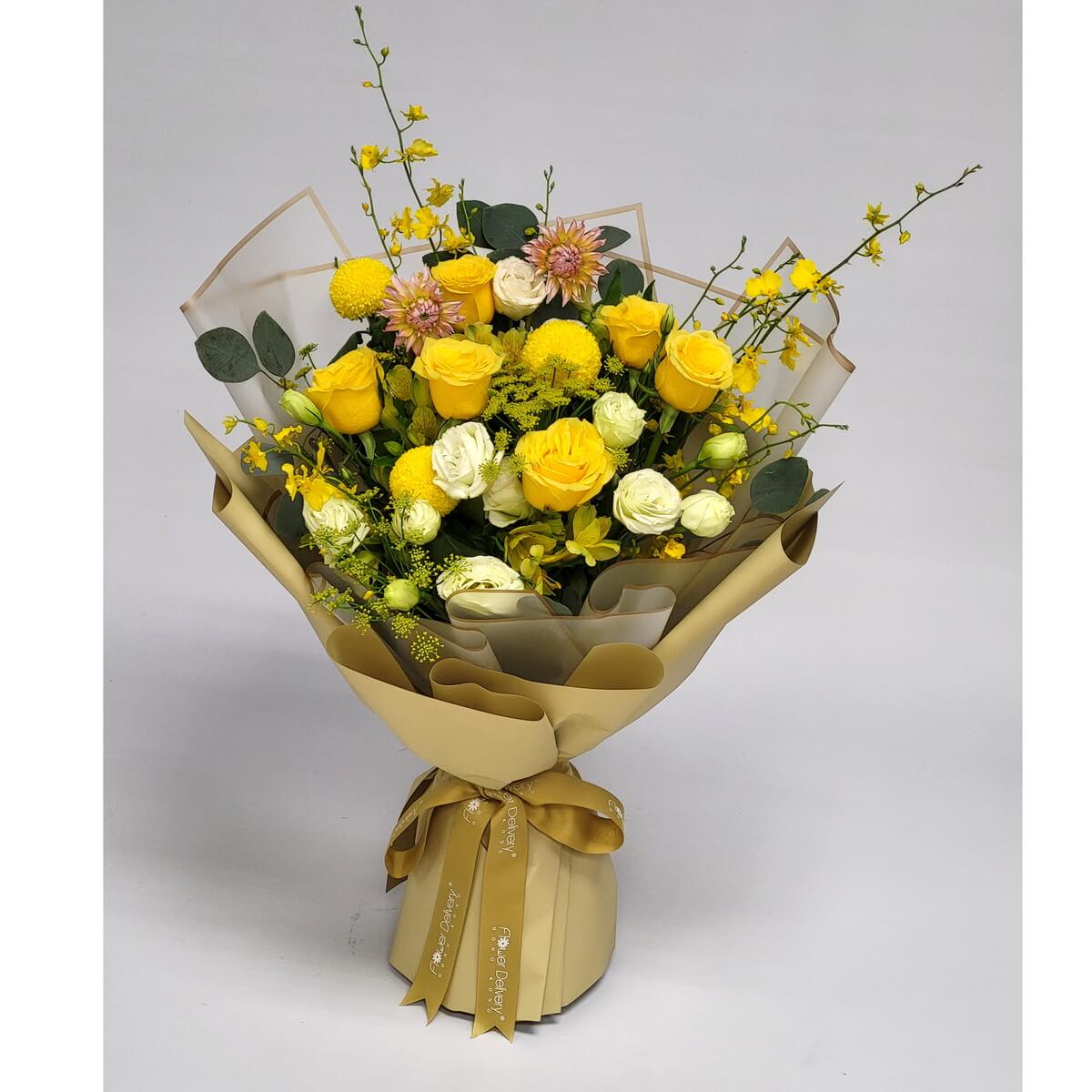 A radiant bouquet of yellow roses, chrysanthemums, orchids, and white eustomas, accented with soft pink blooms and greenery. Wrapped in golden beige paper with matching ribbon. 黃玫瑰、黃菊與洋桔梗交織，洋溢陽光活力，搭配米金包裝展現溫暖氛圍。