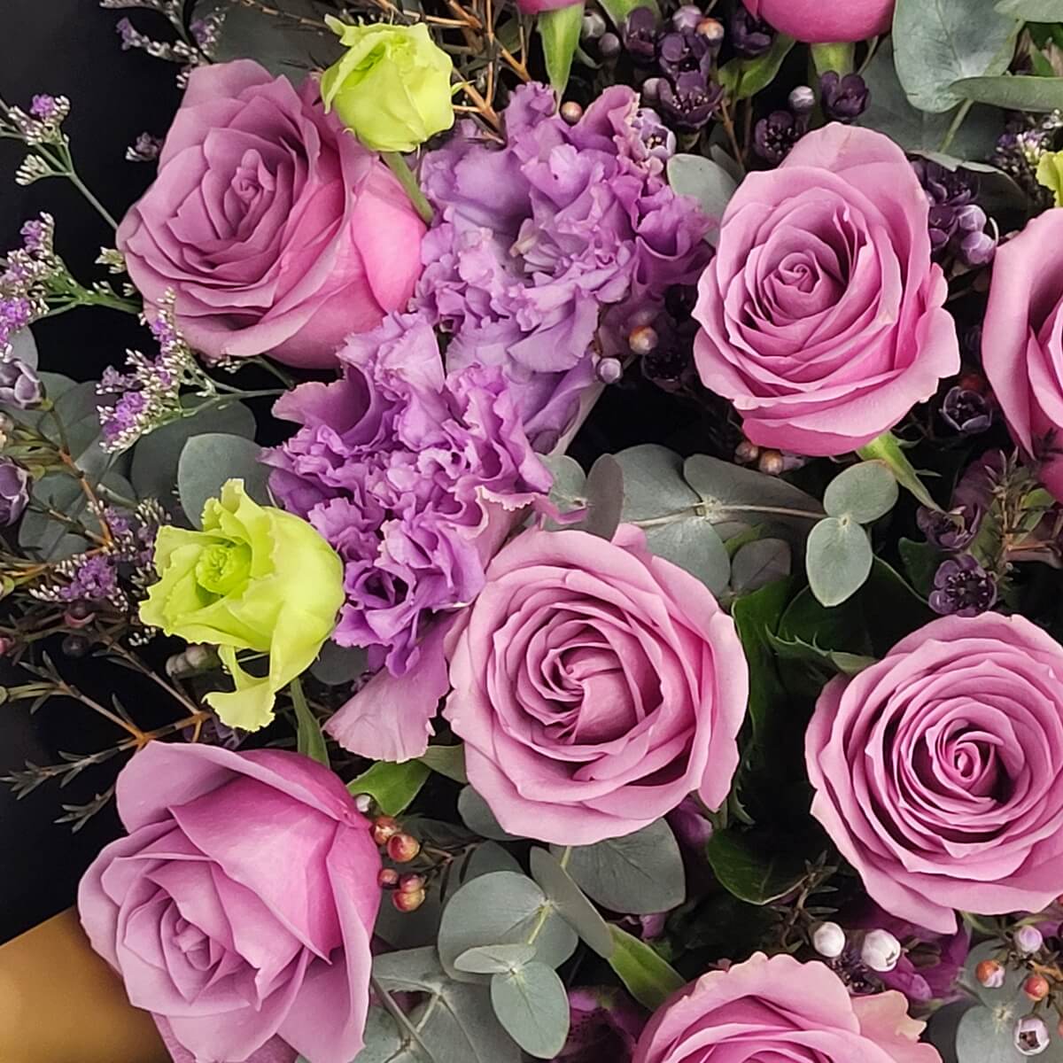 Detail view of a floral mix featuring mauve roses, frilly purple lisianthus, green rosebuds, eucalyptus foliage, and dark wax flower berries - 粉紫玫瑰、皺瓣紫洋桔梗、綠色玫瑰花苞、尤加利葉及深色蠟花果實特寫