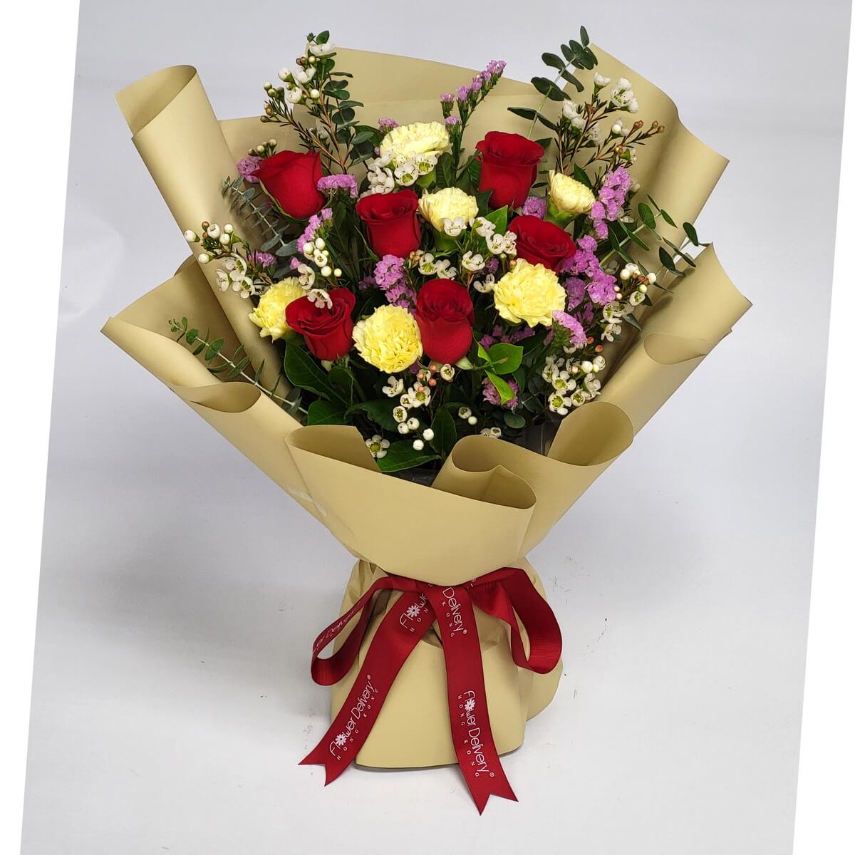 Elegant bouquet with red roses, yellow carnations, purple statice, wax flowers, and eucalyptus, wrapped in champagne gold paper with a red ribbon. 典雅花束，紅玫瑰、黃康乃馨與紫色星辰花交織，配上香檳金包裝與紅絲帶。