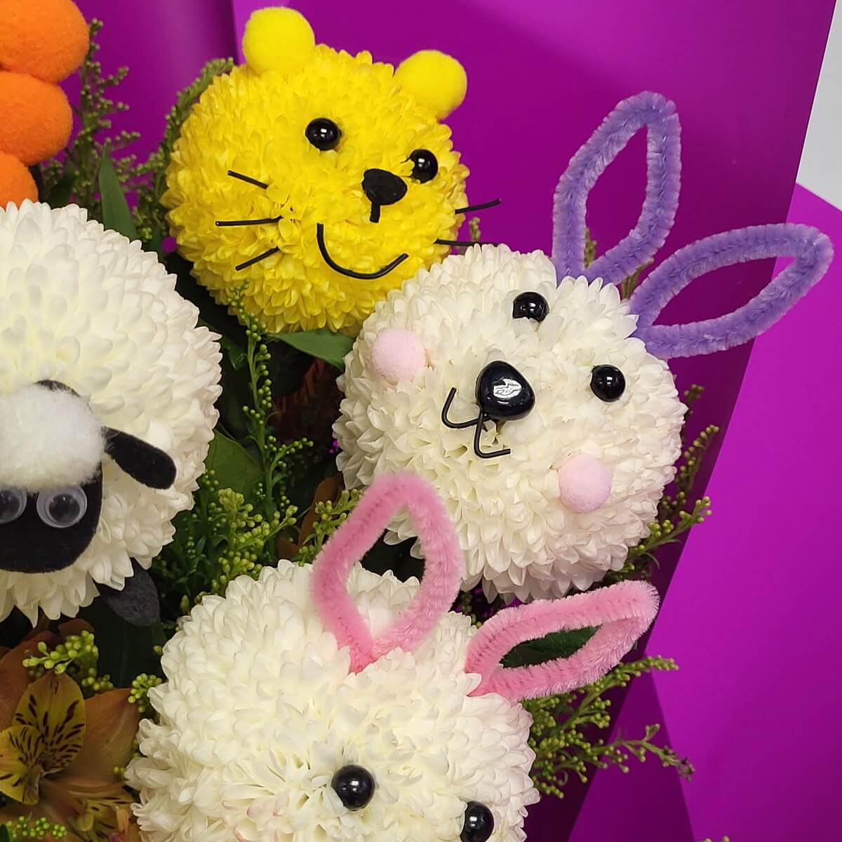 Detail view of rabbit, bear, and sheep faces crafted from white and yellow button chrysanthemums, decorated with pipe cleaners, beads, and felt on green foliage - 白黃乒乓菊製兔子、小熊與綿羊造型，配毛毛條、珠飾及氈材，綠葉襯托特寫