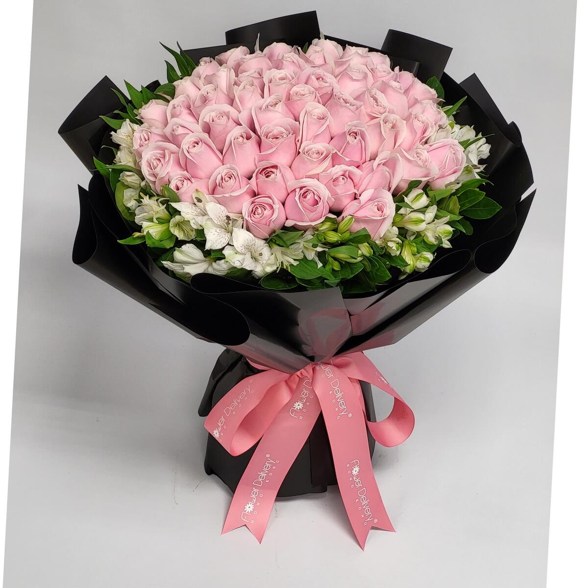 A luxurious bouquet of tightly clustered soft pink roses, encircled with delicate white alstroemeria and greens, wrapped in glossy black paper and finished with a pink ribbon. 粉紅玫瑰環繞潔白花語，優雅而高貴，傳遞真摯愛意。