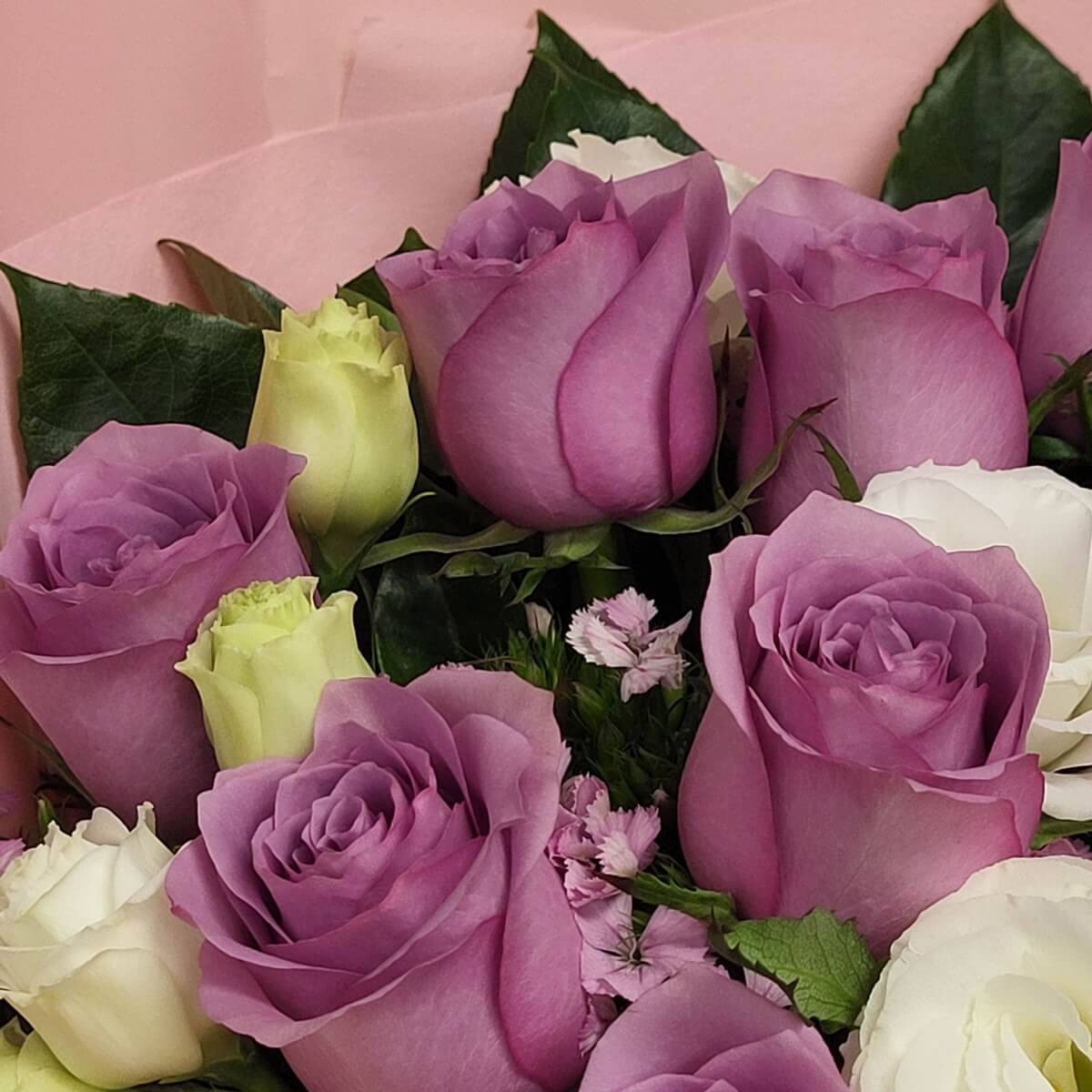 Close-up view of a compact bouquet composed of lavender roses, creamy white and pale green lisianthus buds, arranged with dense layering and natural green foliage for a refined floral presentation 紫色玫瑰、奶白及淡綠洋桔梗花苞近距離花束組合