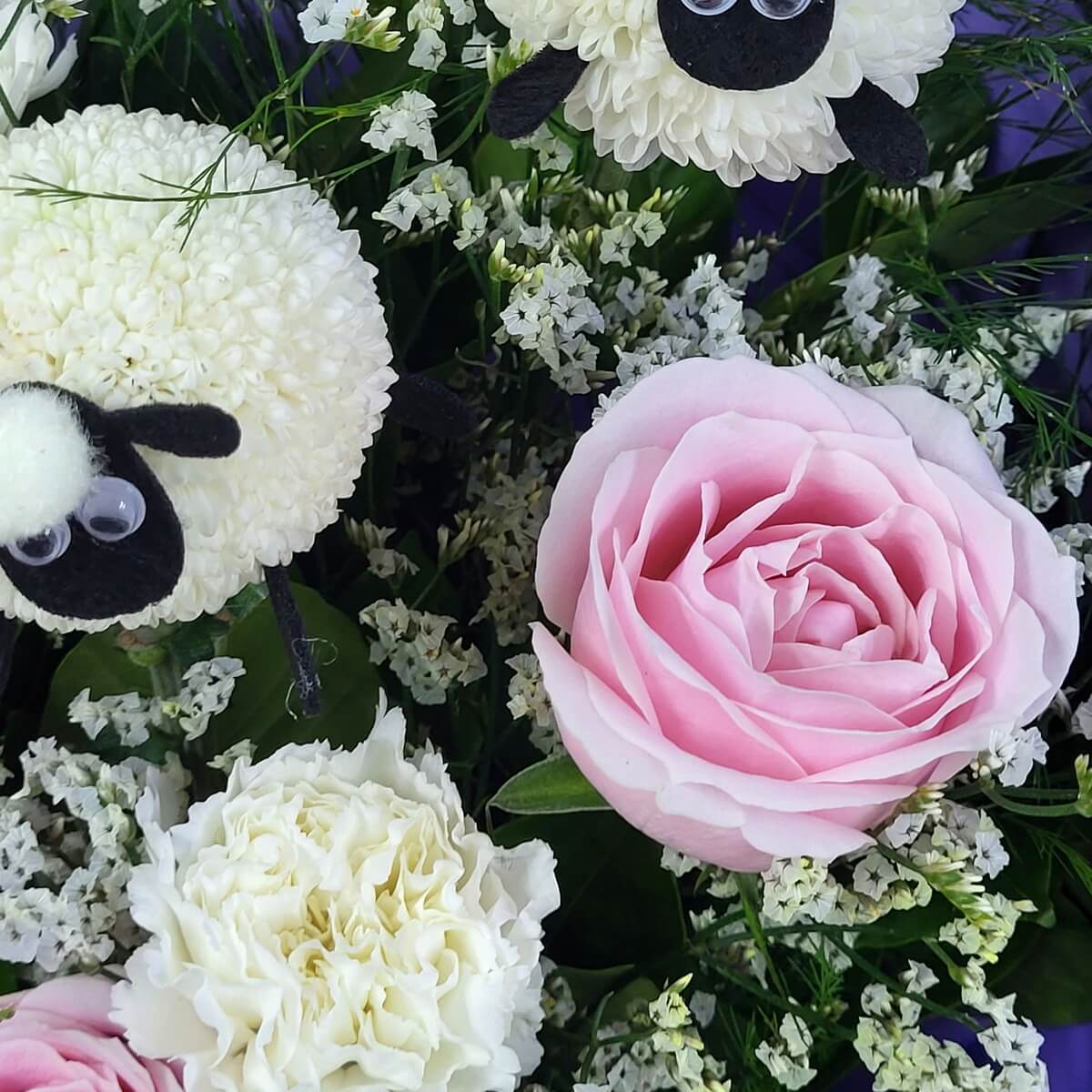 Close-up showing pink rose, creamy white carnation, white statice filler, and novelty sheep figures made from button chrysanthemums 粉紅玫瑰、奶白康乃馨、白情人草及由乒乓菊製成的造型羊偶的特寫畫面