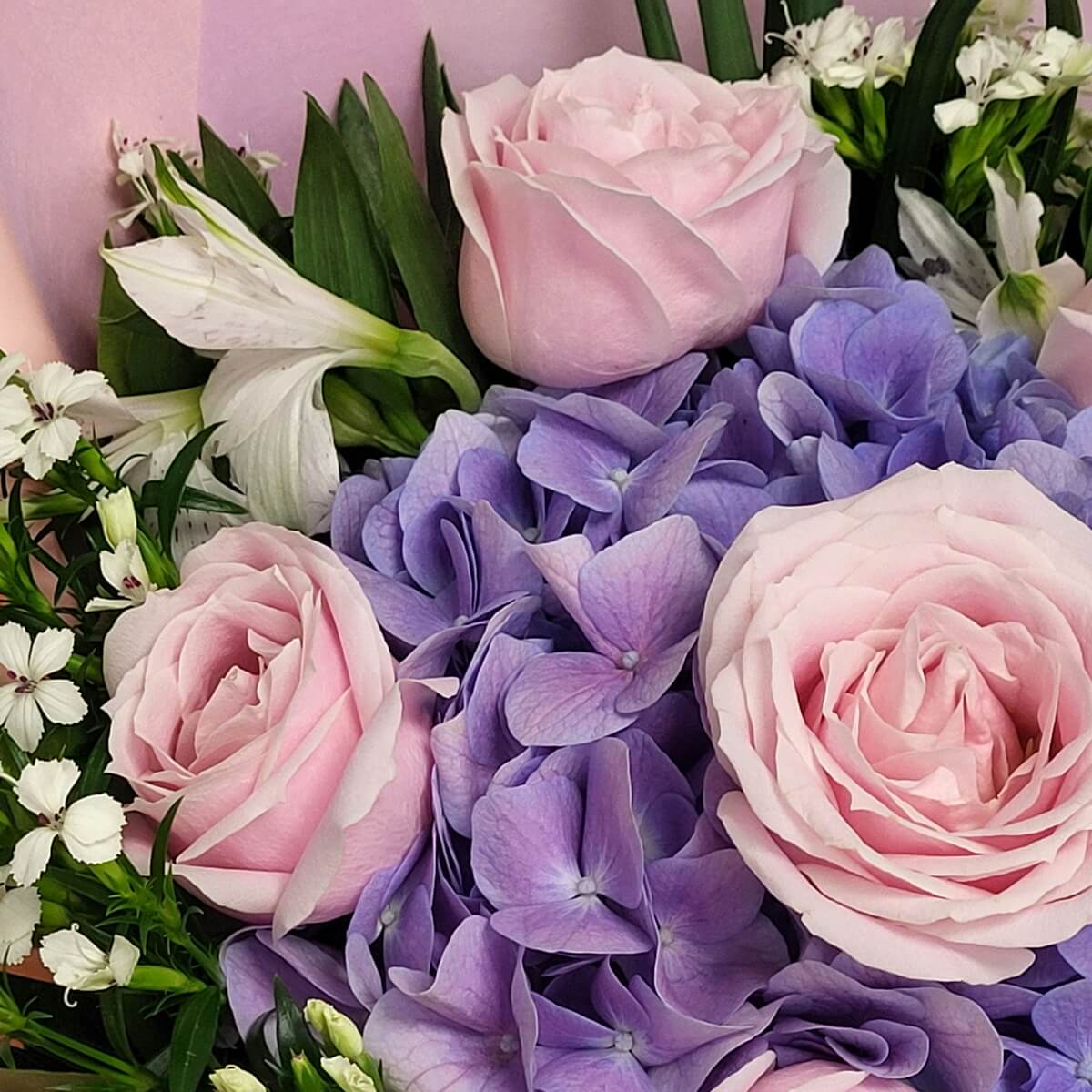 Detail view of pink roses surrounded by purple hydrangeas, white alstroemeria, and petite white dianthus flowers. 粉紅玫瑰、紫繡球花、白色六出花與迷你石竹花的細節特寫。