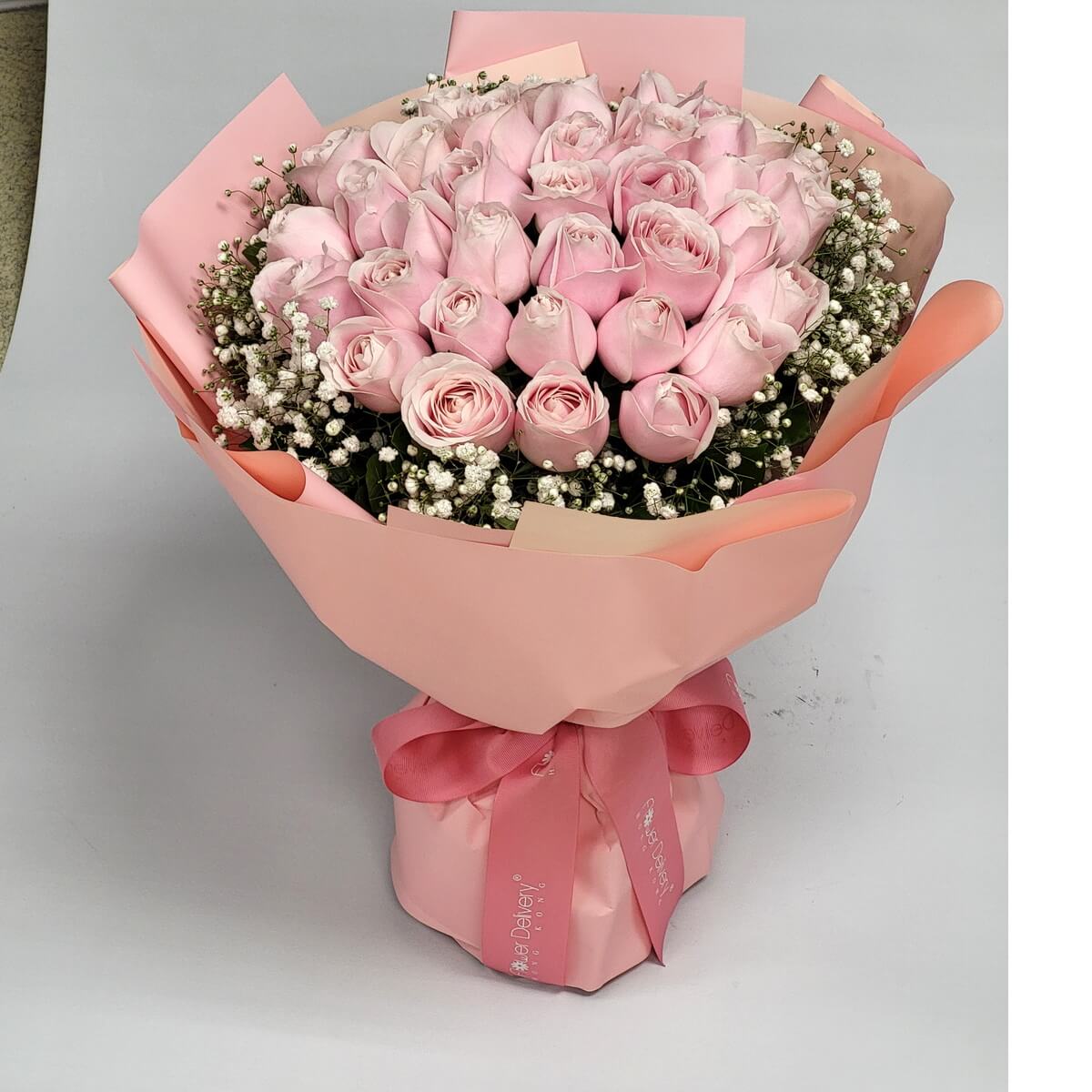 A stunning bouquet of soft pink roses arranged in a dome shape, surrounded by delicate white baby’s breath. Wrapped in matching blush pink paper and ribbon. 淺粉紅玫瑰與滿天星環繞成圓形花束，粉紅包裝與絲帶襯托出溫柔浪漫氣息。