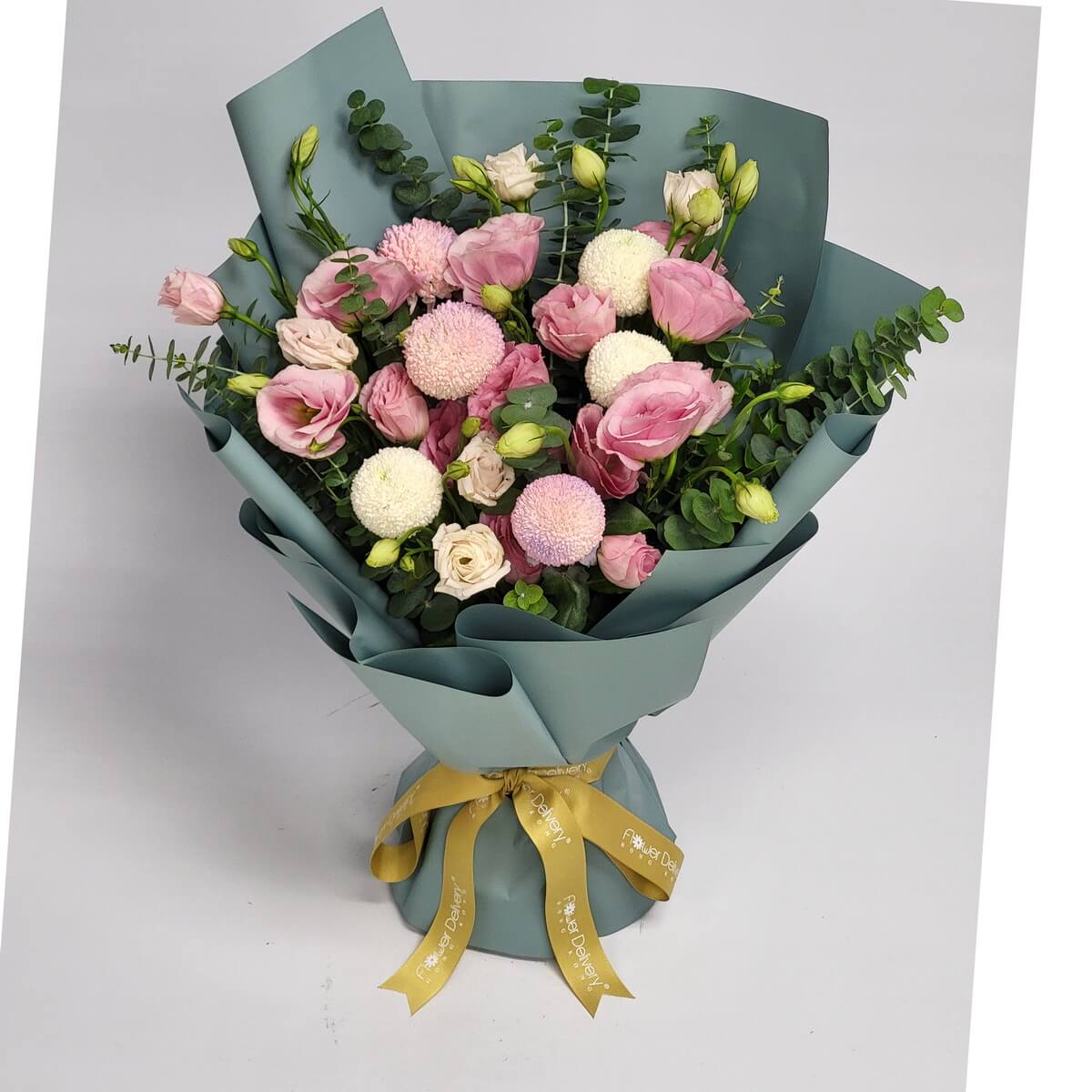 A gentle bouquet of pink and cream eustomas paired with round pastel ping pong chrysanthemums, accented by pale lisianthus buds and eucalyptus. Wrapped in sage green paper with a golden ribbon. 粉紅白色桔梗與乒乓菊交織，搭配尤加利葉，包裹於鼠尾草綠包裝紙與金色絲帶中，柔美而清新。