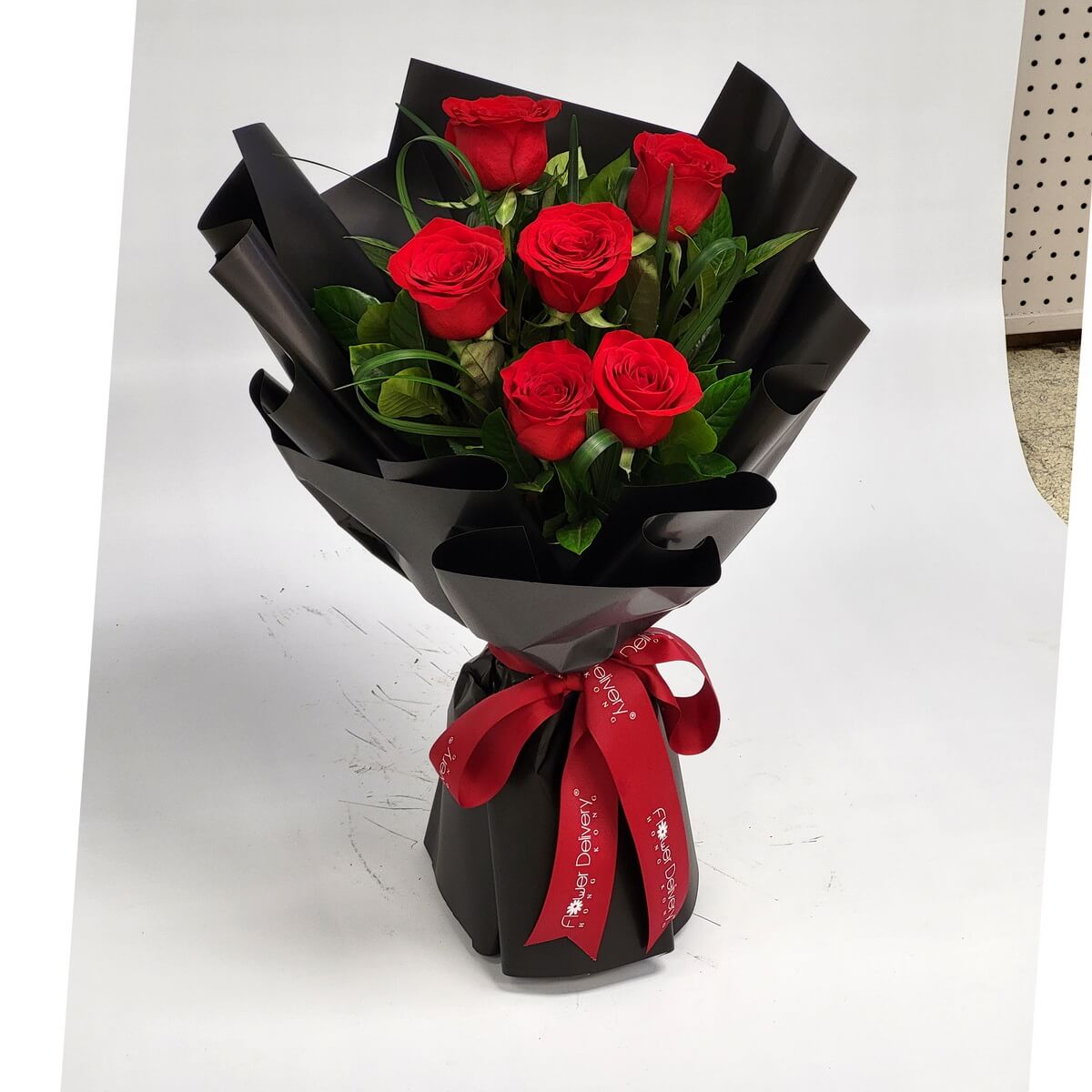 A bold bouquet of six red roses wrapped in elegant black paper with a deep red ribbon. The dramatic contrast exudes timeless romance. 六枝紅玫瑰包裹於黑色包裝紙中，配以酒紅緞帶，經典搭配散發濃濃愛意與神秘魅力。