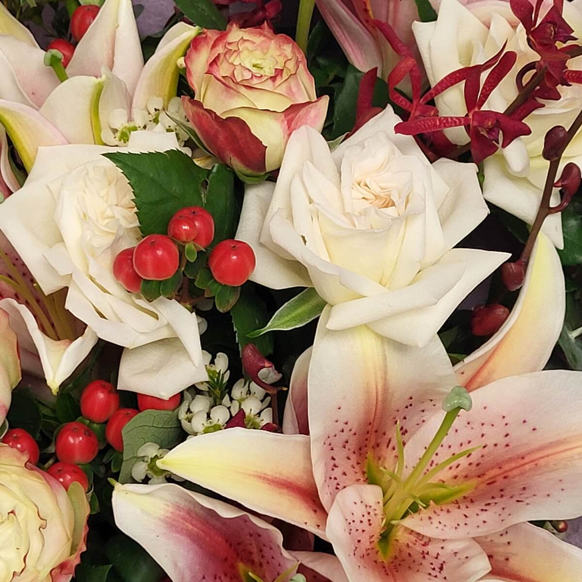 Close-up of ivory roses, blush lilies, red berries, and ranunculus 象牙白玫瑰、淡粉百合、紅色漿果及双色洋牡丹特寫，搭配酒紅色蘭花及白蠟梅。