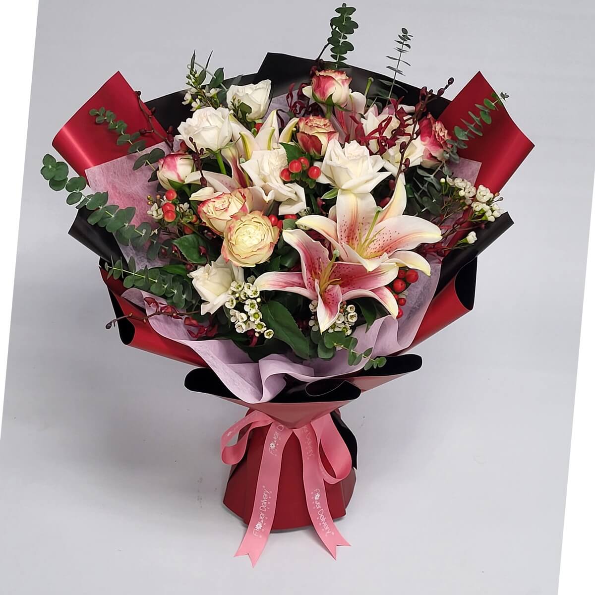 A bold bouquet featuring pink stargazer lilies, ivory and champagne roses, red berries, eucalyptus, and wax flowers, wrapped in red, black, and pink paper with a pink ribbon. 粉百合、香檳與白玫瑰、紅莓與尤加利，搭配紅黑粉包裝與粉色緞帶，展現熱情與高貴。