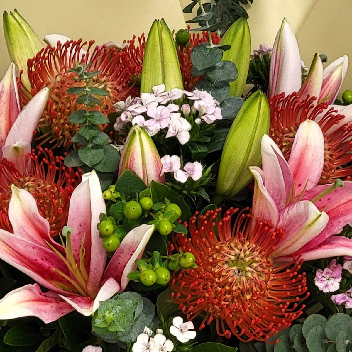 Vibrant pink lilies and red pincushion proteas accented by green berries and soft pink blooms 鮮豔粉百合與紅針墊花搭配綠色果實與柔粉小花，呈現熱情活力的花束設計。
