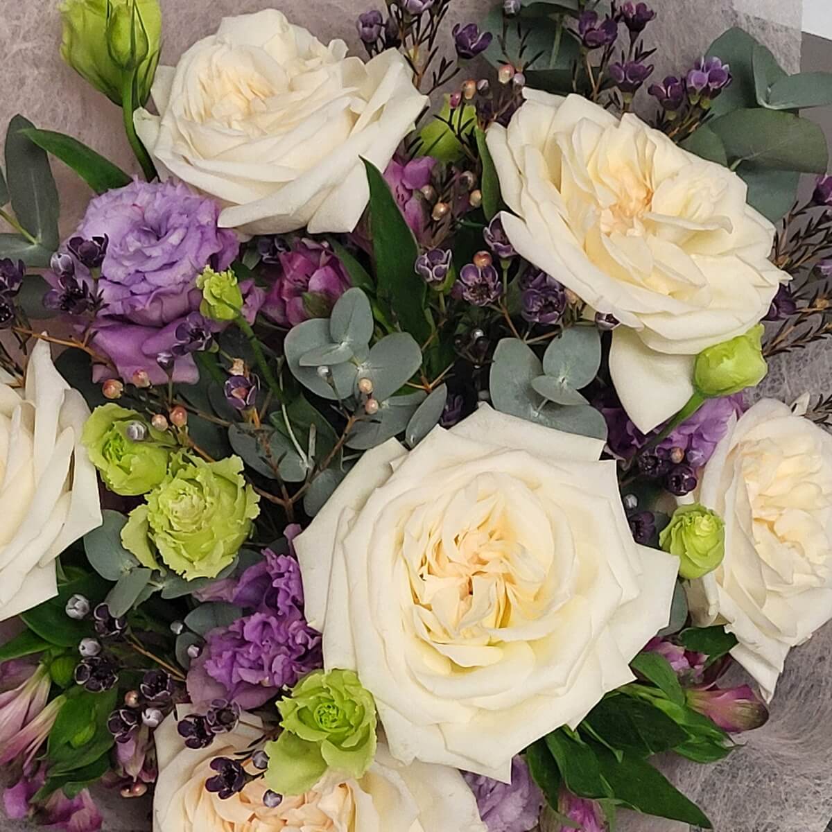 Detail view of soft white garden roses paired with purple lisianthus, green rosebuds, dark purple wax flowers, and eucalyptus leaves wrapped in pale mesh - 白玫瑰配紫洋桔梗、綠玫瑰花苞、深紫蠟花及尤加利葉，淡色網布包裝特寫