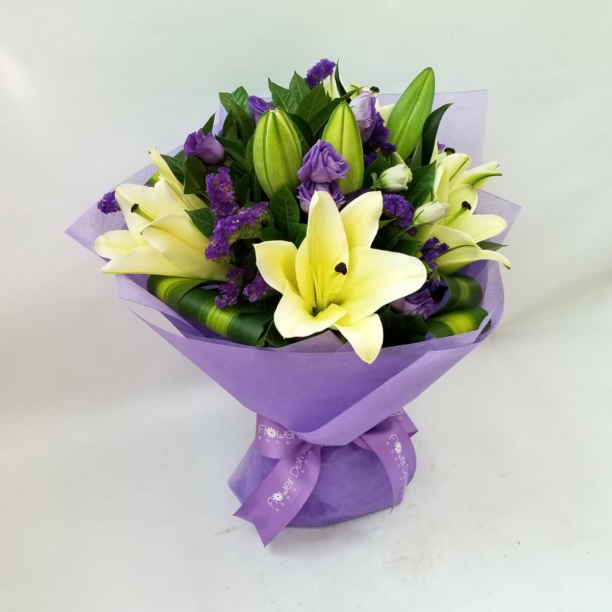 A graceful bouquet of white lilies, lavender roses, and deep purple statice, wrapped in soft purple paper and tied with a matching ribbon. 淡紫包裝中百合與薰衣草玫瑰優雅並列，紫色勿忘我點綴其間。
