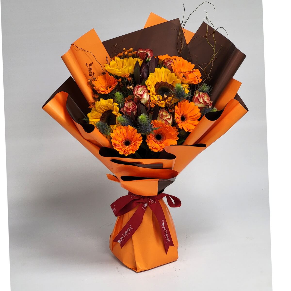 Wrapped bouquet of sunflowers, orange gerbera daisies, bicolour roses, blue eryngium, dark tulips, and orange waxflowers 包裝花束含向日葵、橙非洲菊、雙色玫瑰、藍松蟲草、深鬱金香與橙色蠟花