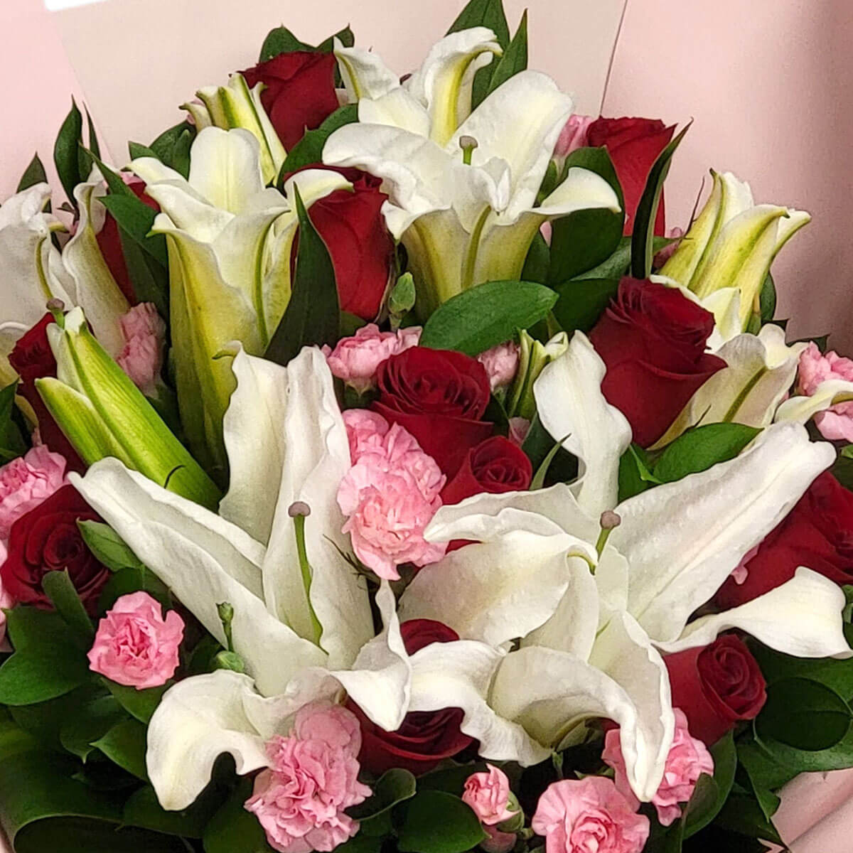 A romantic blend of white lilies, deep red roses, and pink carnations, surrounded by rich green foliage 白百合、紅玫瑰與粉康乃馨交織出浪漫氛圍，綠葉相襯，優雅迷人。