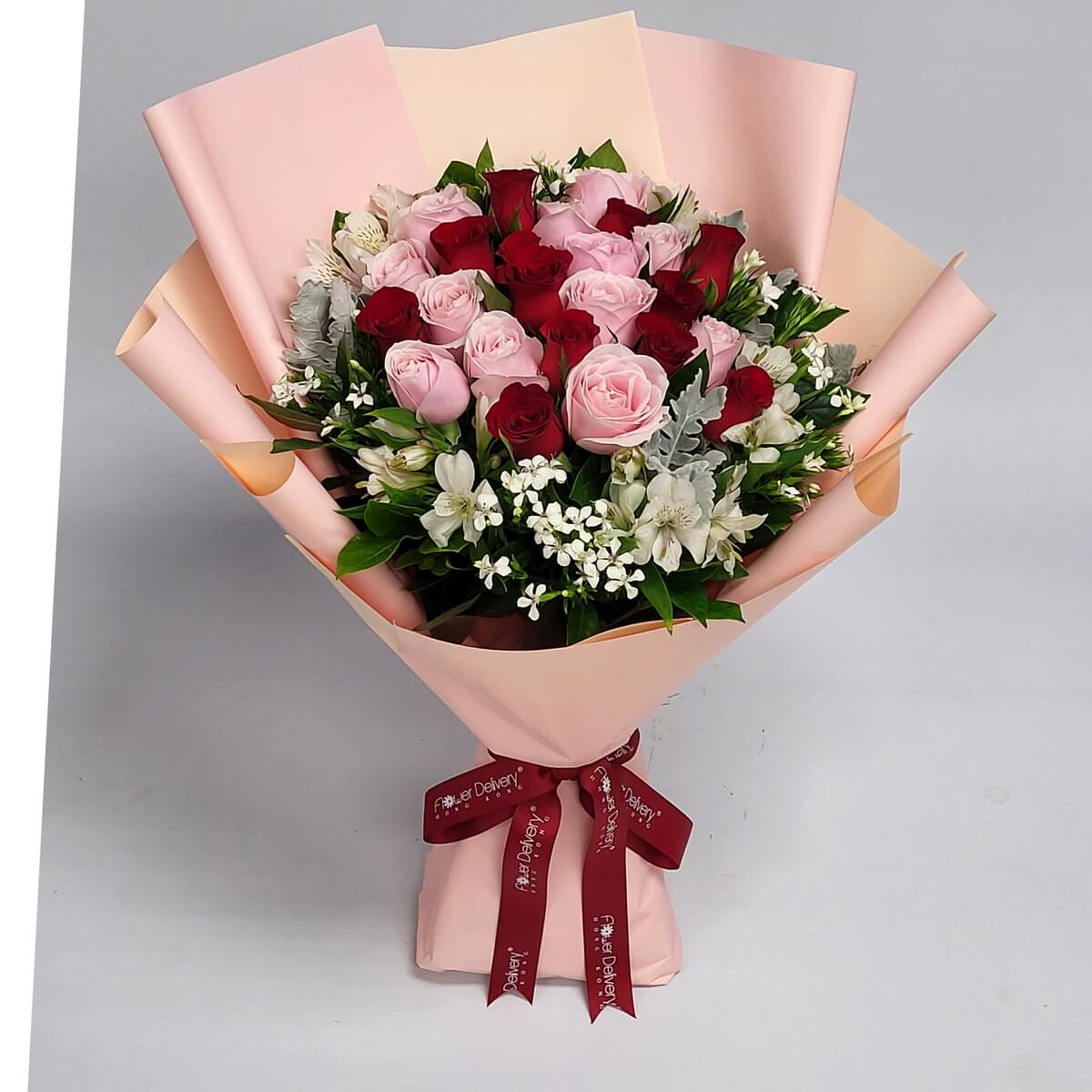 Bouquet of pink and red roses with white accent flowers, wrapped in champagne paper and tied with a burgundy ribbon. A romantic and harmonious arrangement. 淡粉與紅玫瑰搭配白色花點綴，香檳包裝配酒紅絲帶，浪漫協調。
