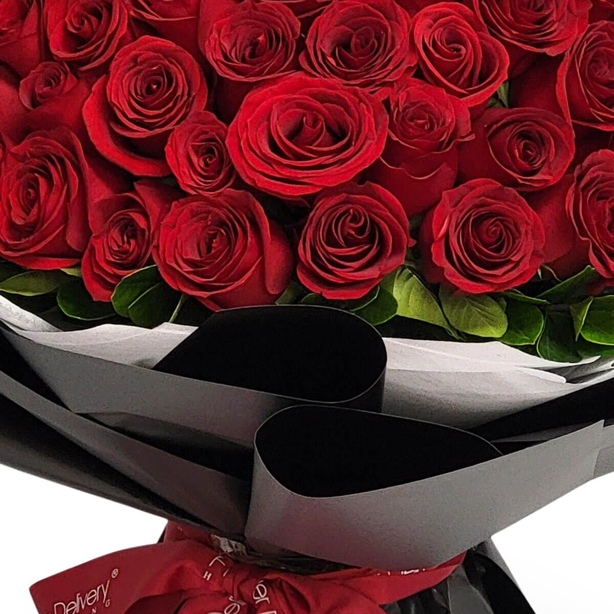 Hand-tied bouquet of red roses with green foliage, presented in black and white wrapping with a red ribbon. 紅玫瑰配綠葉手綁花束，以黑白包裝紙包裹，綁上紅絲帶。