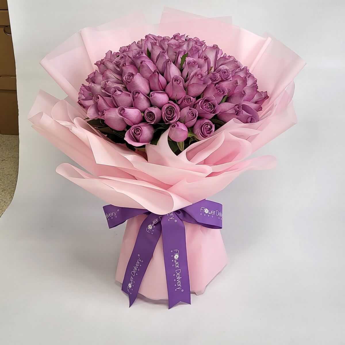 Lavish bouquet of lavender-purple roses wrapped in soft pink paper with a violet ribbon. Romantic and graceful. 華麗薰衣草紫玫瑰花束，配粉紅包裝紙與紫絲帶，優雅浪漫。