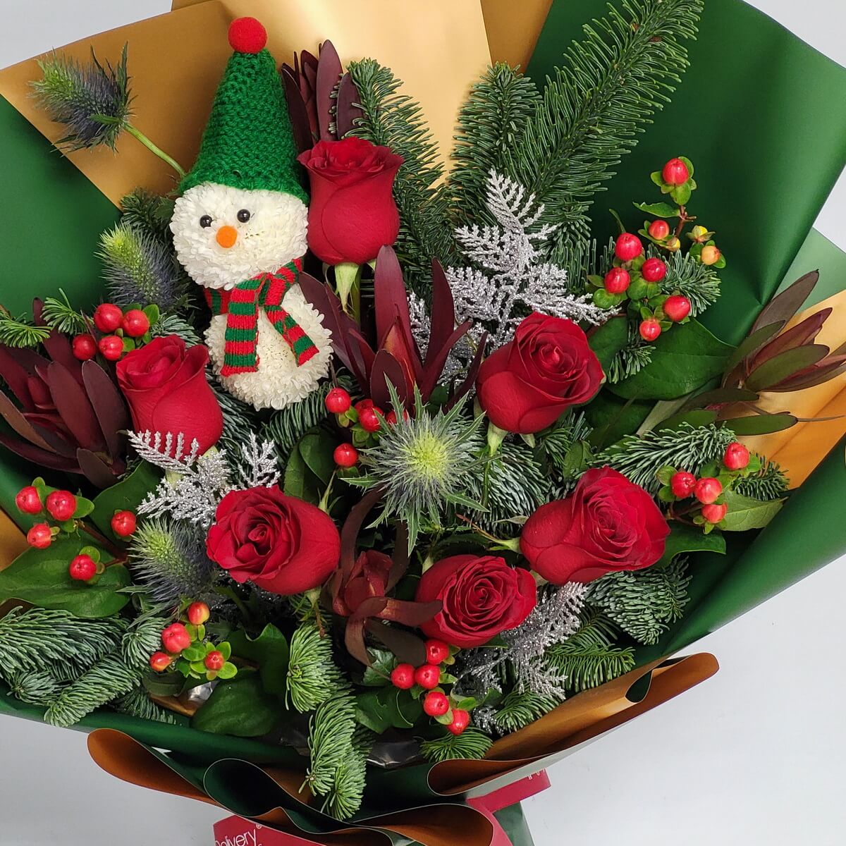 Festive bouquet featuring red roses, blue eryngium, red hypericum berries, pine greenery, and a snowman made from white button chrysanthemums - 節日花束含紅玫瑰、藍刺芹、紅繡球果與白色乒乓菊雪人