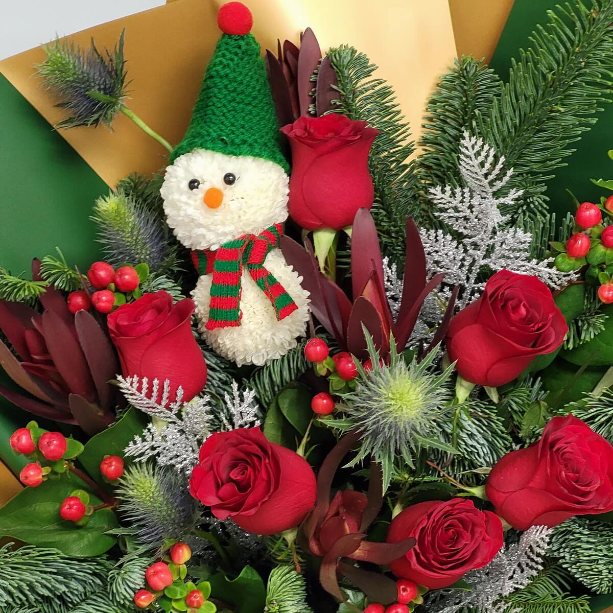 Close-up view of a bouquet with red roses, blue eryngium, red hypericum berries, fir branches, and a snowman made from white button chrysanthemums - 花束特寫含紅玫瑰、藍刺芹、紅繡球果、冷杉與乒乓菊雪人