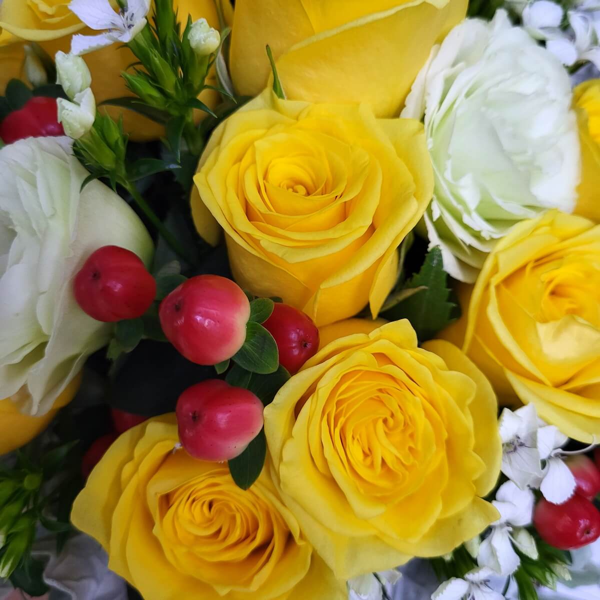 Close-up of vibrant yellow roses mixed with white lisianthus, red hypericum berries, and white filler blooms. | 鮮黃玫瑰搭配白桔梗、紅色繡球果與白色配花的特寫圖像。