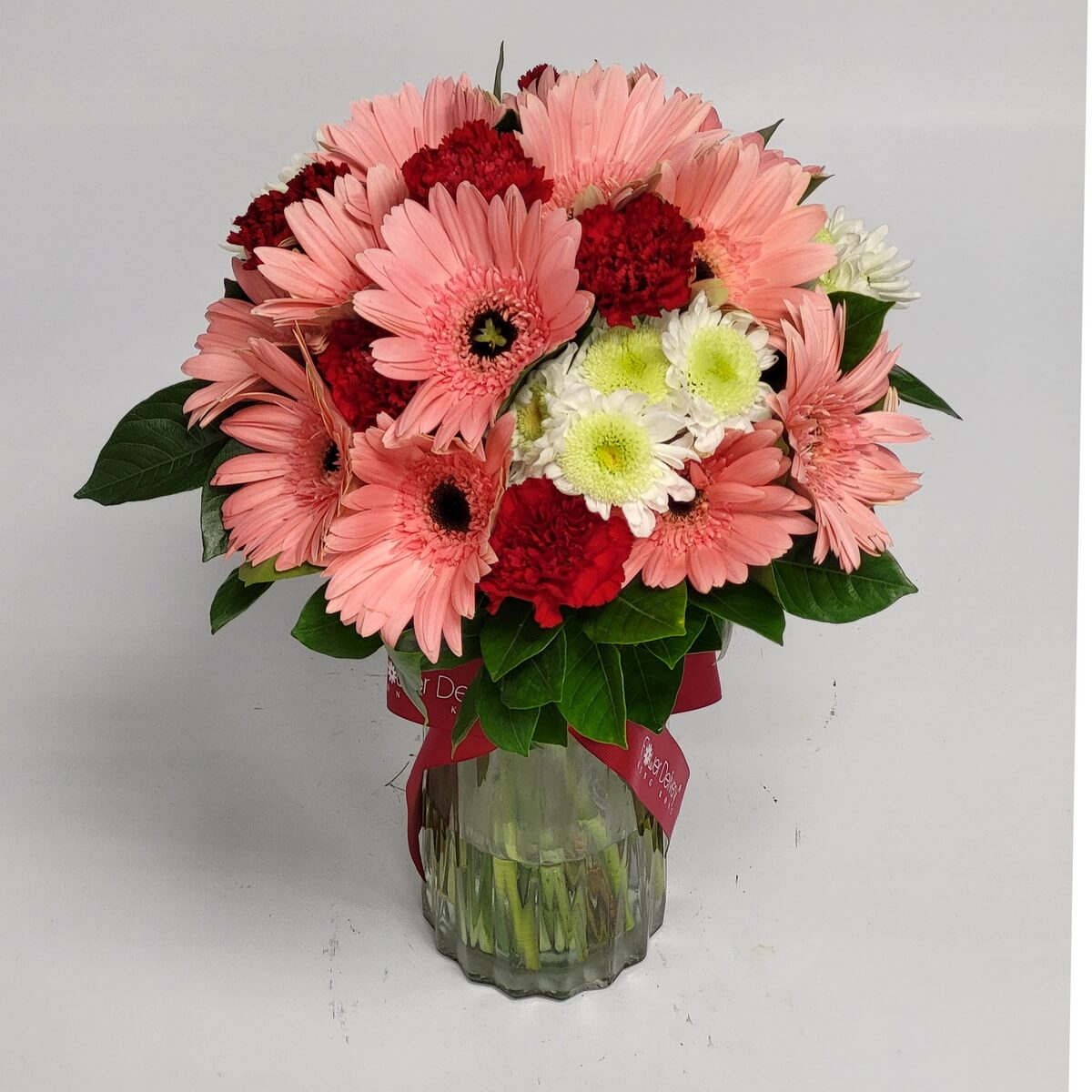 Full arrangement with pink gerberas, red carnations, and white-green button chrysanthemums in a ribbed glass vase 粉紅非洲菊、紅康乃馨與白綠乒乓菊整體插花於直紋玻璃瓶中