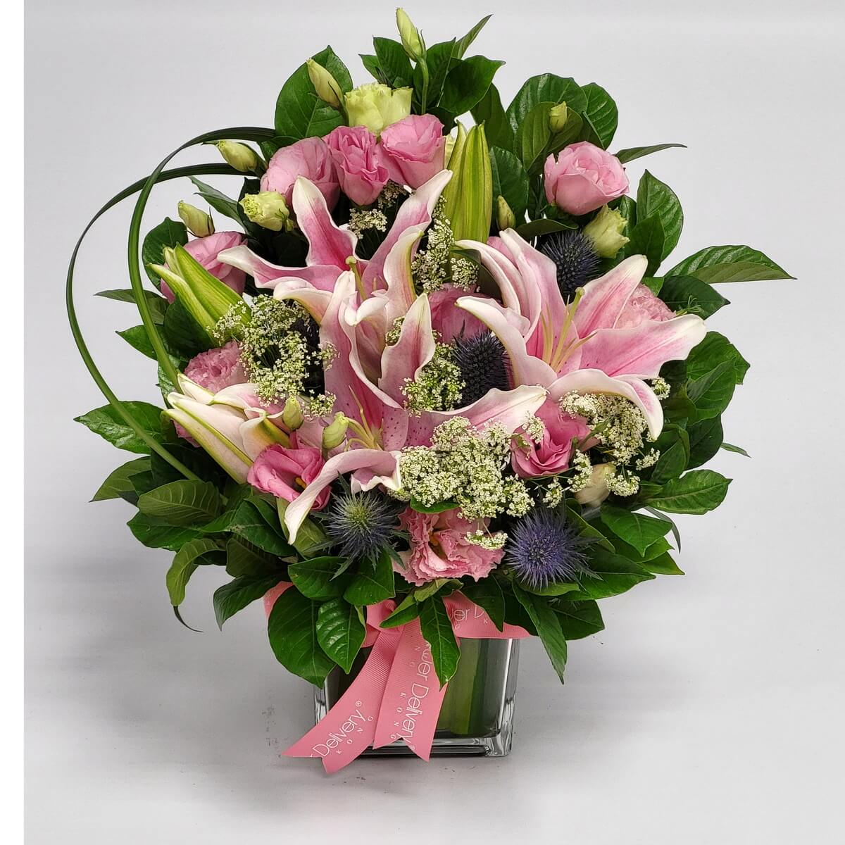 Pink lilies, roses, lisianthus with Queen Anne’s lace & thistles 粉紅百合、玫瑰、洋桔梗搭配蕾絲花與藍色薊花，營造柔美中帶有個性的花藝風格，放置於玻璃方瓶中，粉色緞帶點綴。