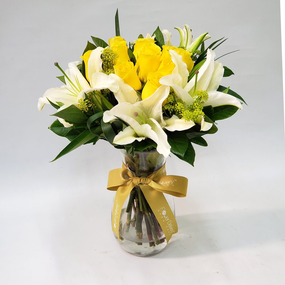 Original photo of vase arrangement featuring yellow roses, white lilies, green filler flowers, and mixed greenery, tied with gold ribbon - 黃玫瑰、白百合、綠色配花與襯葉配金色絲帶的玻璃瓶插花