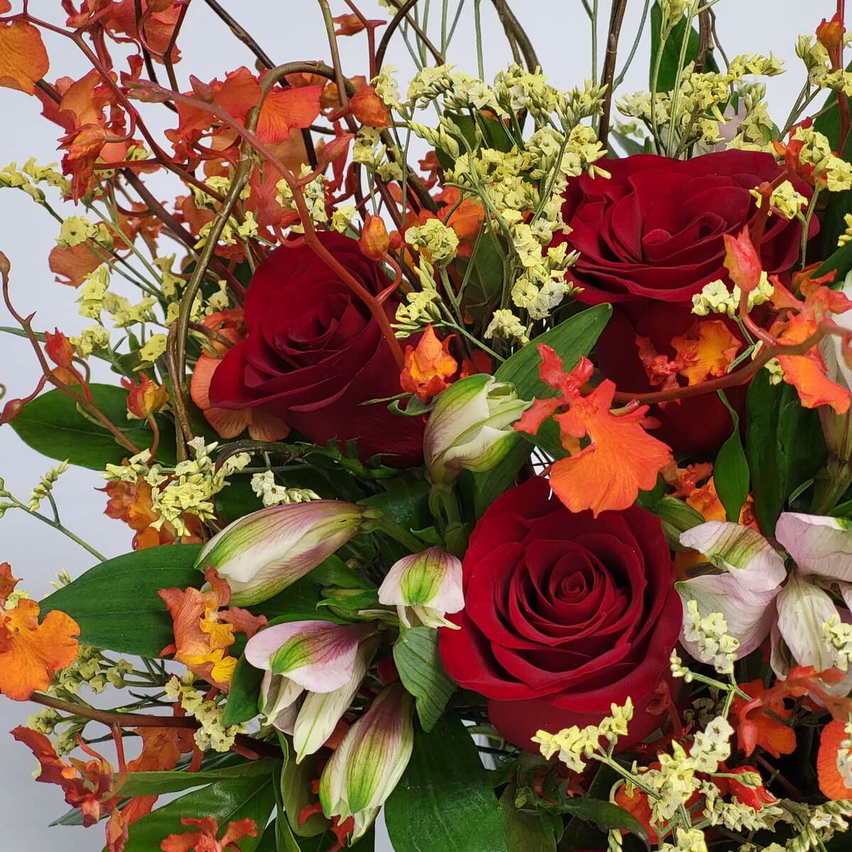 Detail view of red roses, vibrant orange dancing orchids, pale pink alstroemeria, and yellow statice with greenery 紅玫瑰、橙跳舞蘭、粉紅六出花與黃蠟菊及綠葉細節呈現