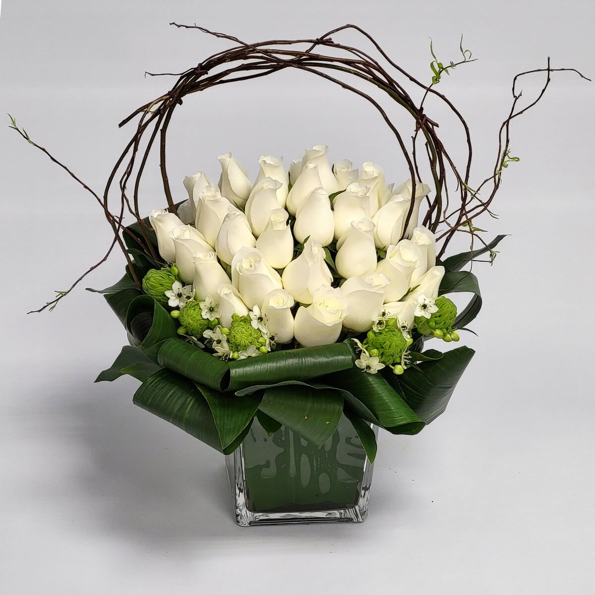 Elegant white rose design 典雅白玫瑰搭配綠色花材與捲曲柳條，方形玻璃瓶襯以大葉包圍，線條簡潔，氣質脫俗，是展現純潔與尊重的完美花禮。