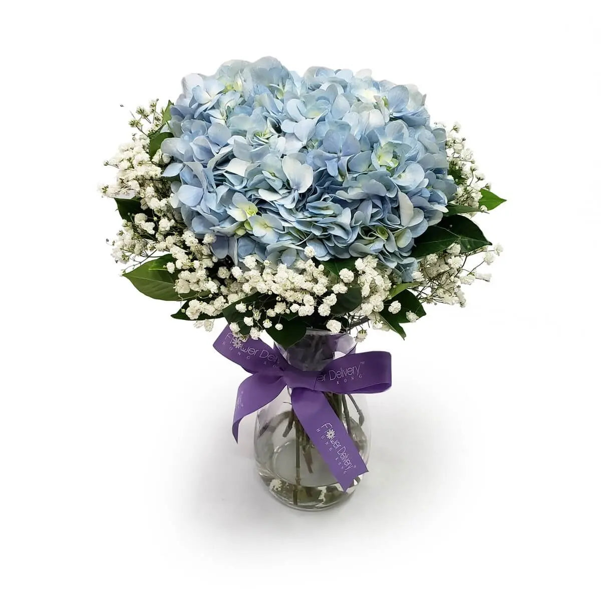 Tightly clustered blue hydrangeas accented with white baby's breath and glossy greenery in a vase with purple ribbon | 繡球花與滿天星緊密搭配，襯以翠綠葉材，裝於透明玻璃瓶中，綁上紫色絲帶，清雅脫俗。