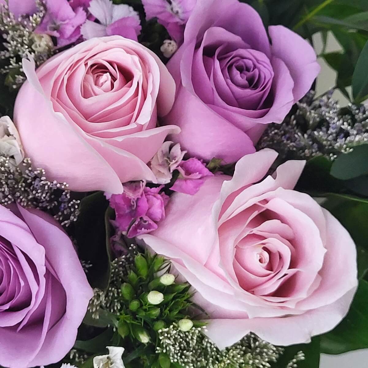 Zoomed-in view of pink and lavender roses surrounded by baby’s breath, limonium, and assorted greenery | 粉紅與紫玫瑰近拍，襯以滿天星、花旗松與綠葉點綴。