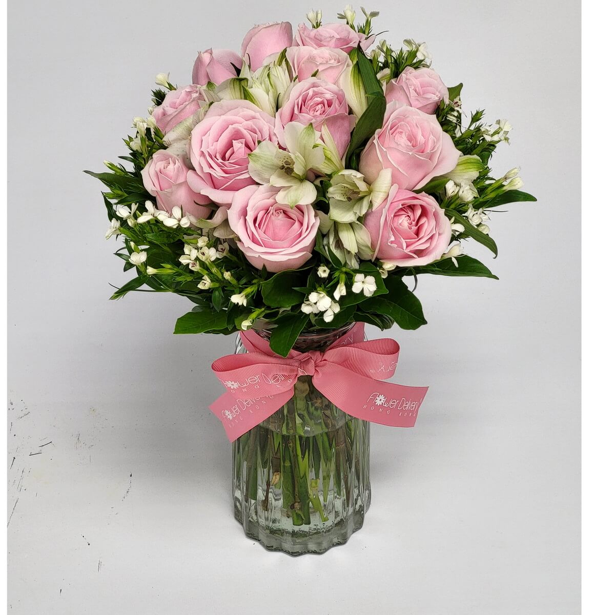 Pink roses with white filler flowers 粉紅玫瑰搭配白色小花與綠葉，插於雕花玻璃瓶中，粉紅絲帶點綴，洋溢甜美浪漫氣息，適合表達溫柔心意。
