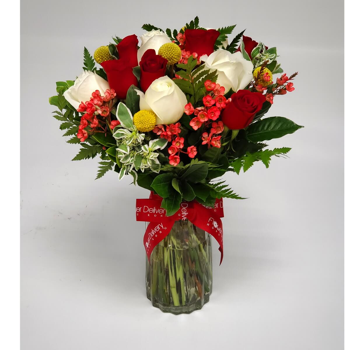 Red and white roses with coral blooms and craspedia in a vase 紅白玫瑰與黃球菊、珊瑚色小花巧妙搭配，襯以綠葉，插於透明玻璃瓶中，綁紅色絲帶，營造熱情與優雅兼具的氛圍。