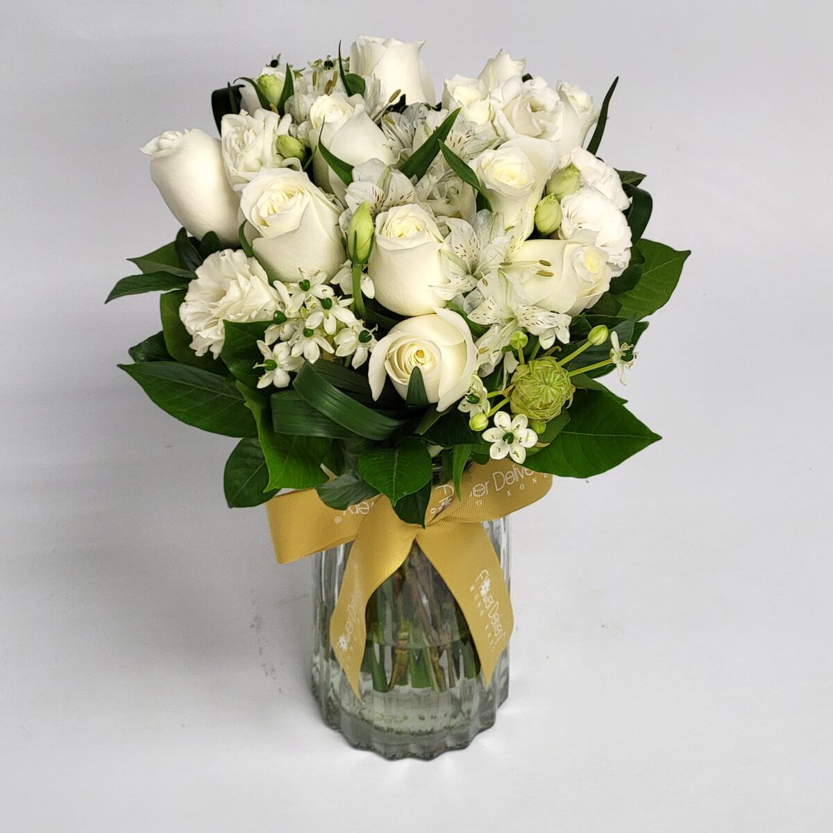 Elegant all-white bouquet with roses and fillers in a vase 優雅純白玫瑰、小玫瑰與百合，搭配葉材與白色襯花，插於玻璃花瓶中，配金色絲帶，簡潔高貴。