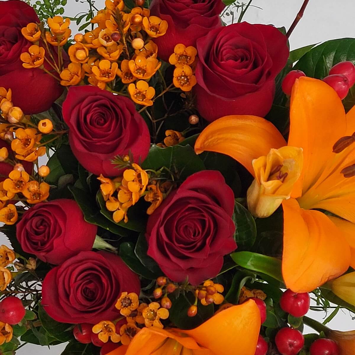 Zoomed-in floral detail of red roses surrounded by orange Asiatic lilies, yellow wax flowers, and red berries - 紅玫瑰配橙色亞洲百合、黃色蠟花與紅漿果的花藝細節特寫