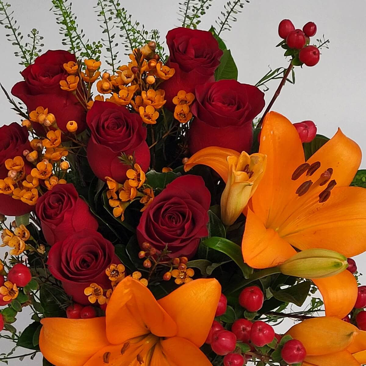 Close-up floral view featuring red roses, bright orange lilies, and red hypericum berries - 紅玫瑰、橙百合及紅色貫葉連翹果特寫