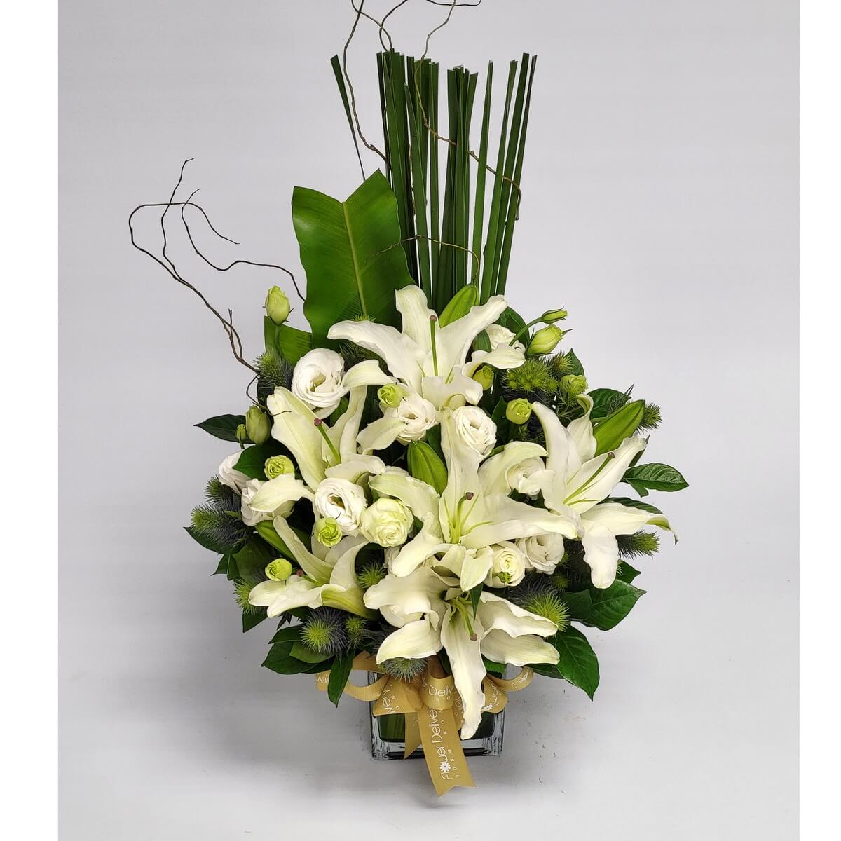 Modern floral arrangement with white lilies, lisianthus, blue thistle, green buds, tall foliage, and curly branches in square glass vase 白百合、洋桔梗、藍松球、綠花苞、高葉材與彎枝組合方形玻璃瓶現代花藝