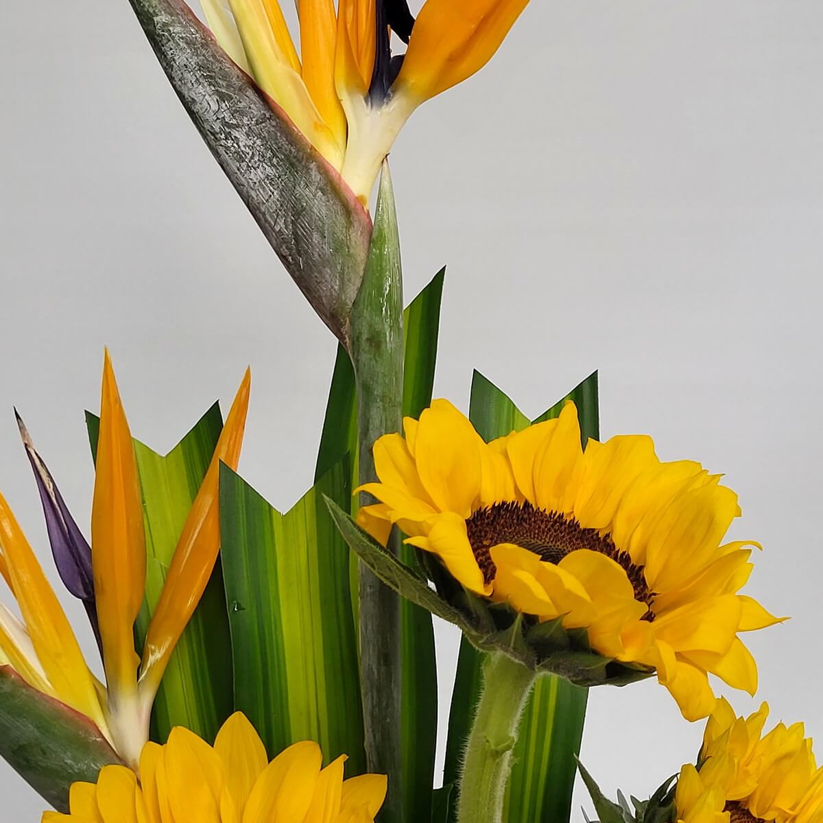 Detail view of bold sunflowers and bird of paradise blooms, complemented by striped tropical leaves in a vertical composition 向日葵與天堂鳥花配以條紋熱帶葉材構成立體直線花藝細節特寫