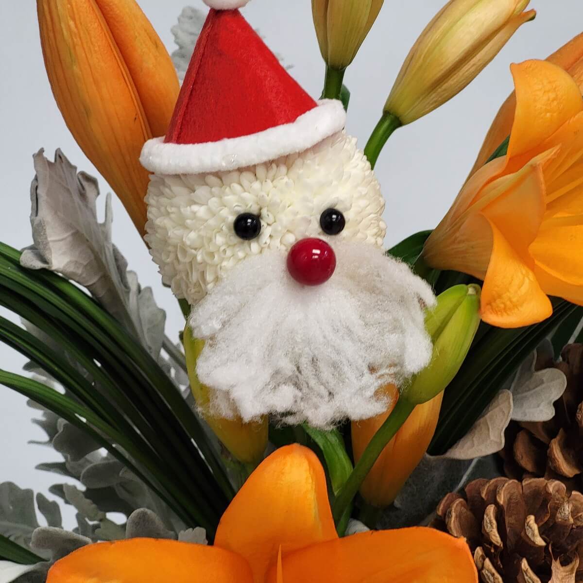 Close-up of Santa face crafted from white button chrysanthemums, surrounded by orange Asiatic lilies and pinecones - 白色乒乓菊聖誕老人造型，配橙色百合與松果特寫