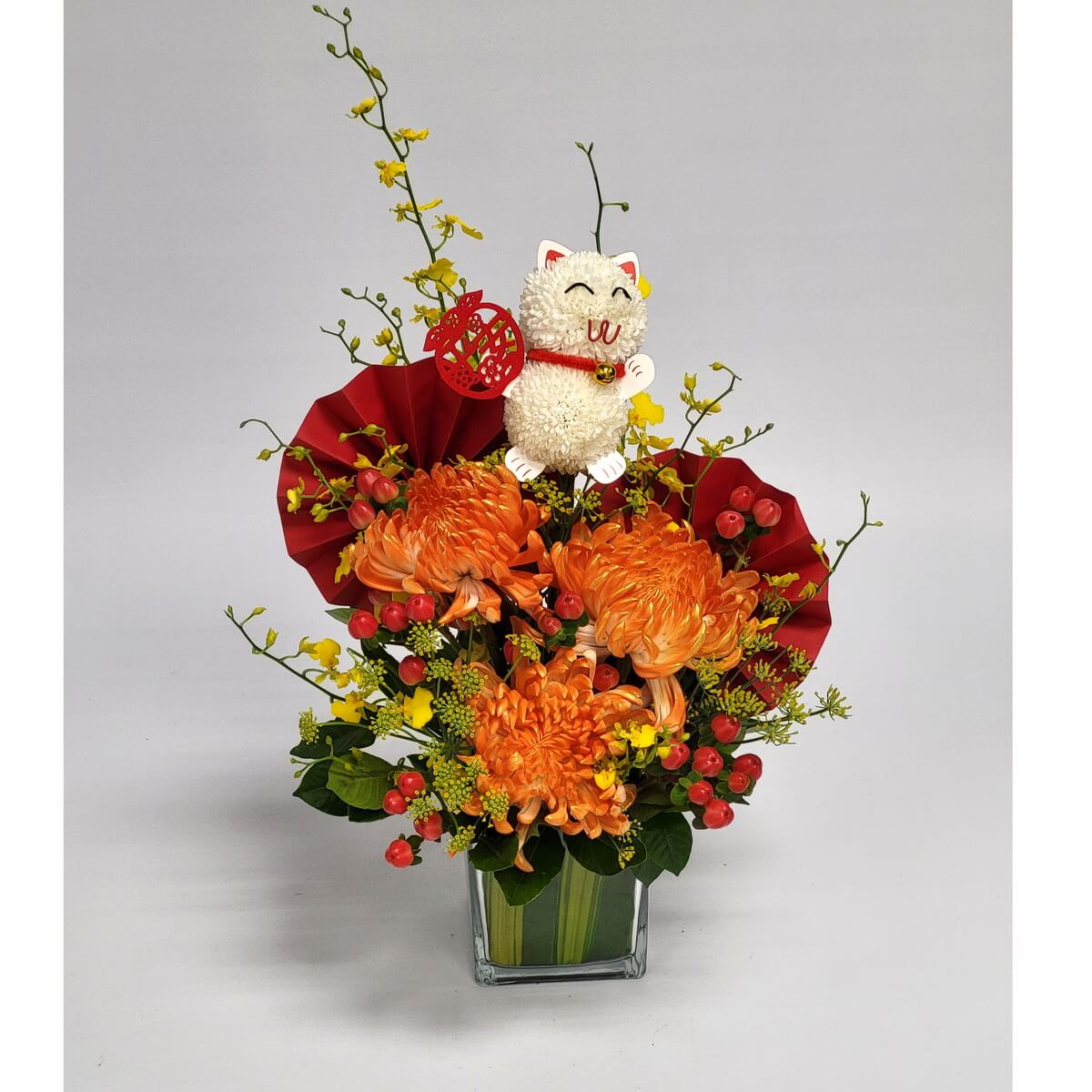 Glass vase with orange chrysanthemums, yellow oncidium orchids, red hypericum berries, red fan accents, and a cat decoration 玻璃花瓶設計，橙色菊花搭配舞春蘭、紅色漿果、摺紙扇及可愛招財貓擺件，色彩喜慶。