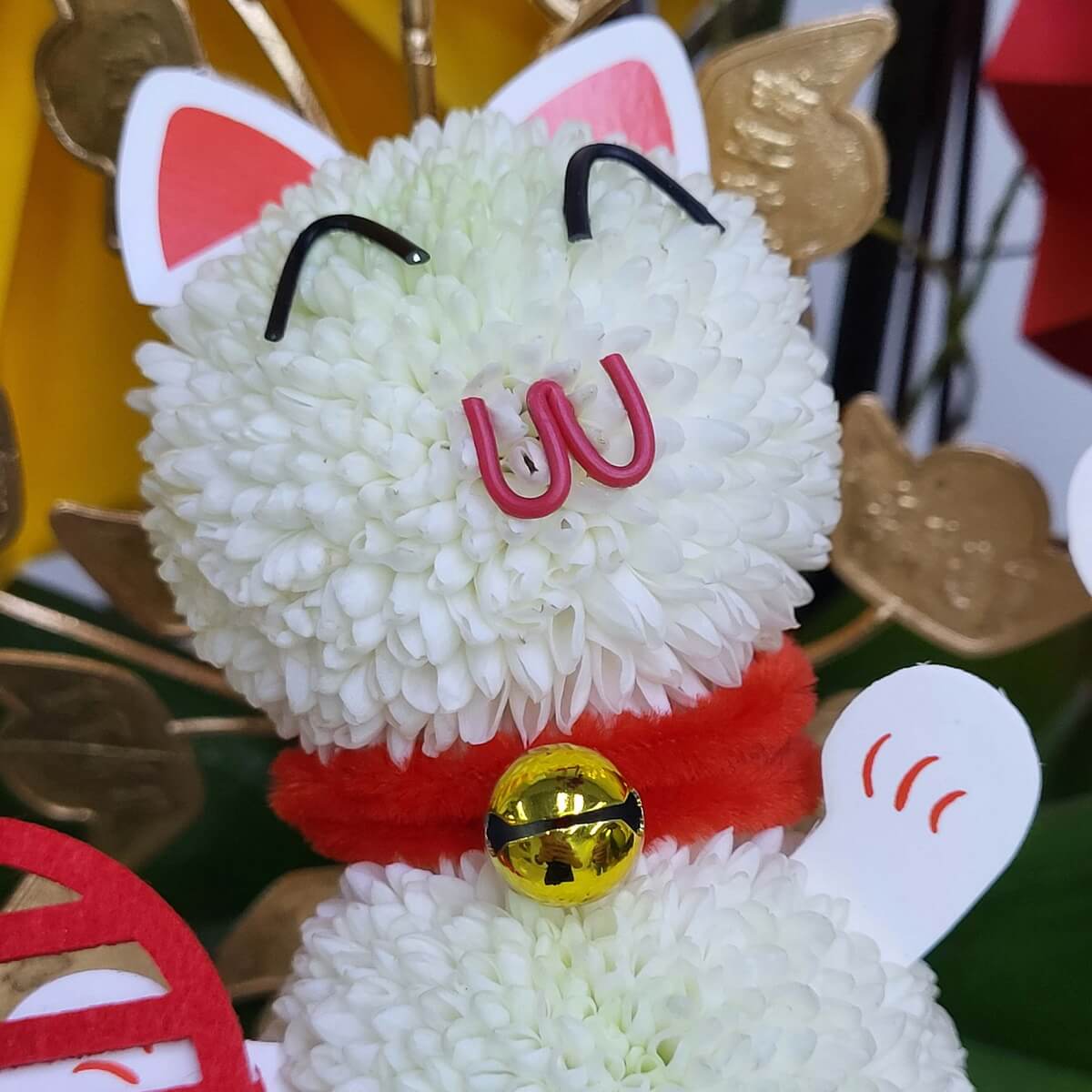 Detail view of a lucky cat figure crafted from white button chrysanthemums, featuring pink nose, red collar, and gold bell 白乒乓菊打造的招財貓造型細節特寫，配粉紅鼻、紅色頸圈與金鈴飾件
