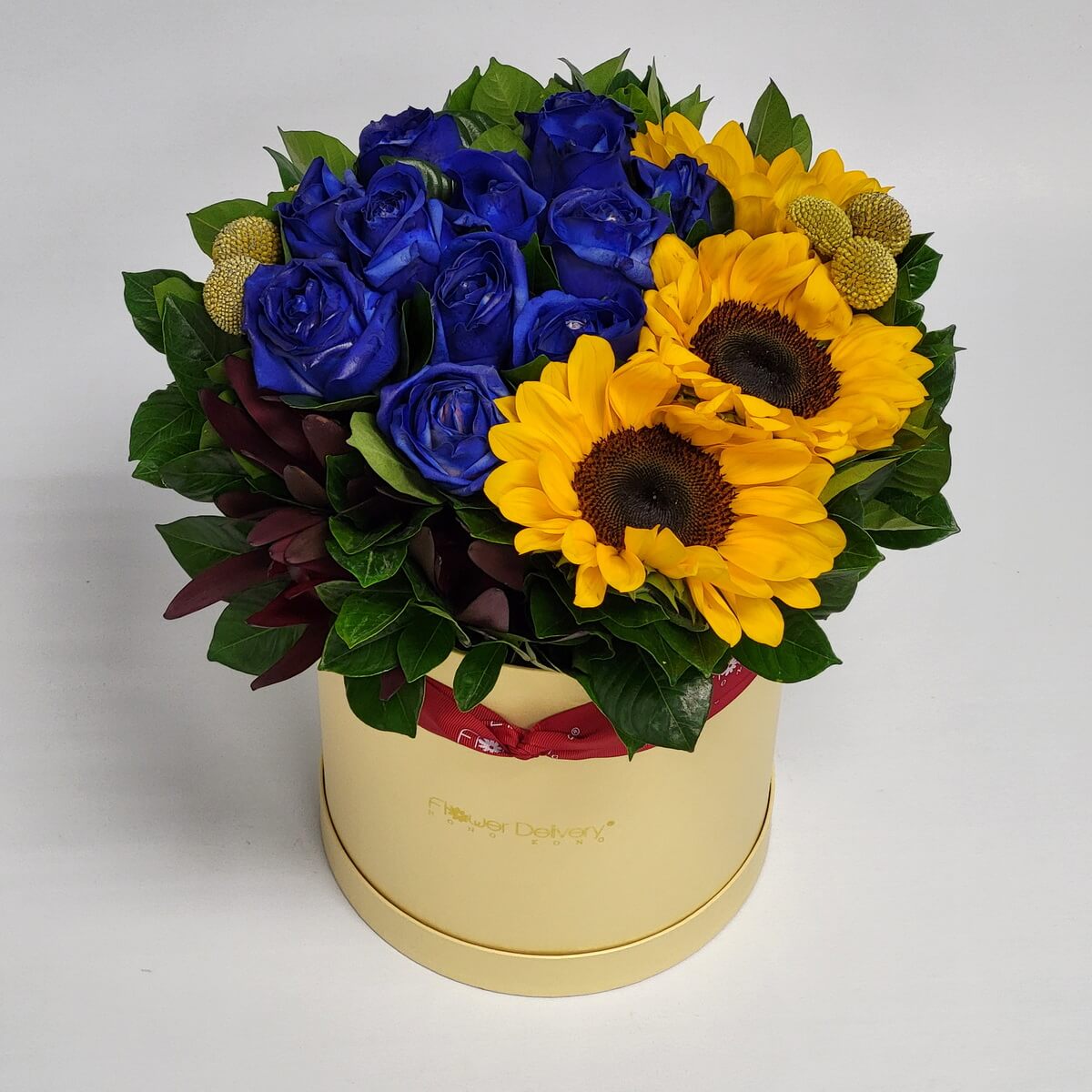 Box arrangement with deep blue roses, bright yellow sunflowers, craspedia, and mixed greenery in a round pale yellow hatbox 圓形淺黃花盒內插深藍玫瑰、亮黃色向日葵、金球花與多種葉材構成的設計花藝