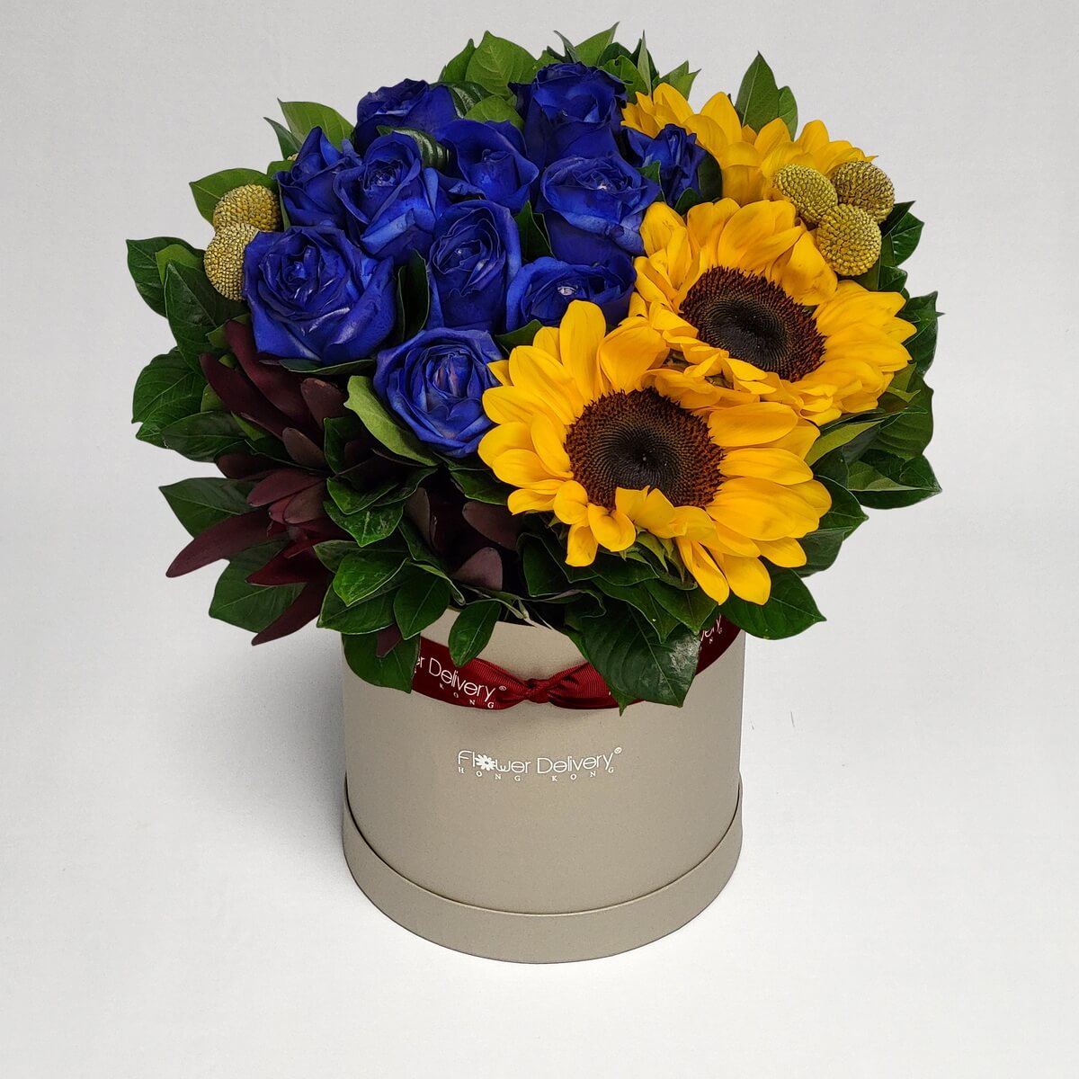 Real photo of hat box flower arrangement with blue roses, yellow sunflowers and button chrysanthemums with green foliage - 藍玫瑰、向日葵與乒乓菊帽盒花藝配綠葉
