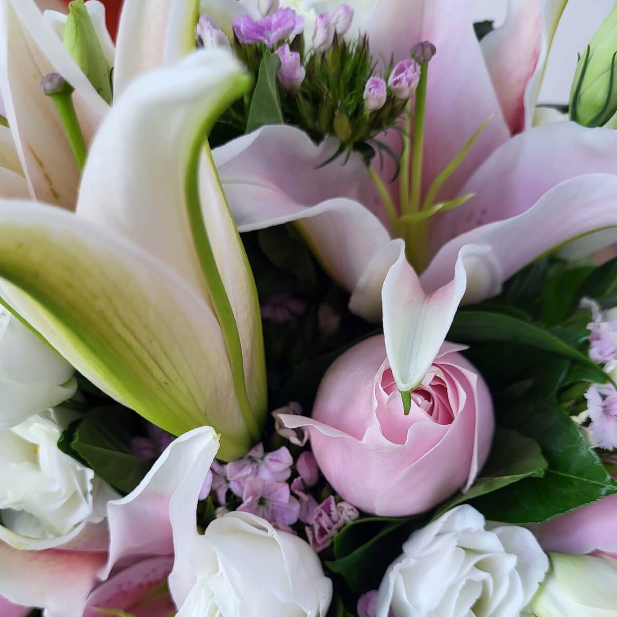 Detailed view of pink lilies, light pink rose, white lisianthus, and purple filler blooms with greenery | 粉紅百合、淡粉玫瑰、白色桔梗及紫色配花特寫，配以綠葉襯托