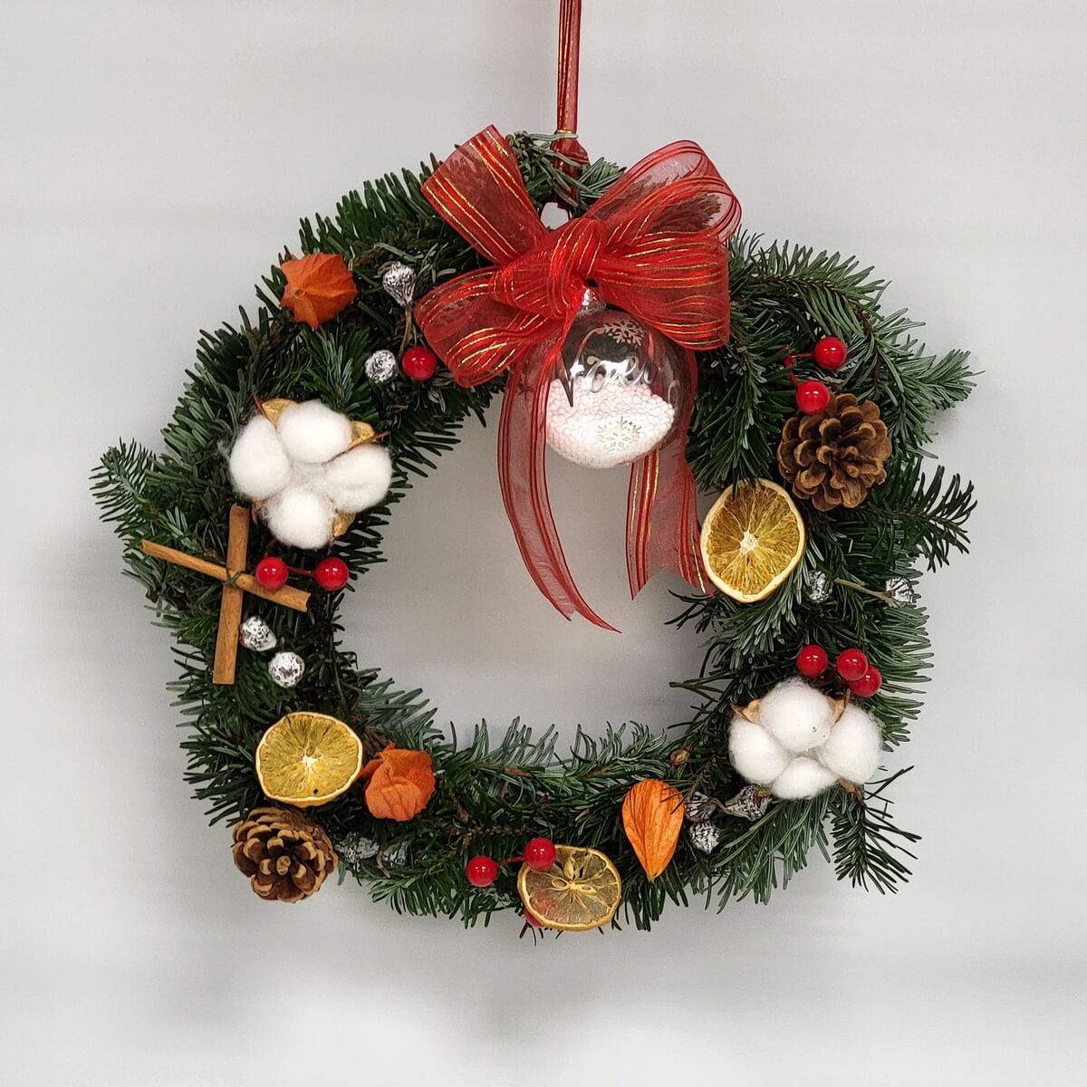 Decorative evergreen wreath featuring cotton blooms, pinecones, red berries, dried citrus, and a red bow 常綠裝飾花圈配棉花、松果、紅莓、乾柑橘及紅色蝴蝶結。